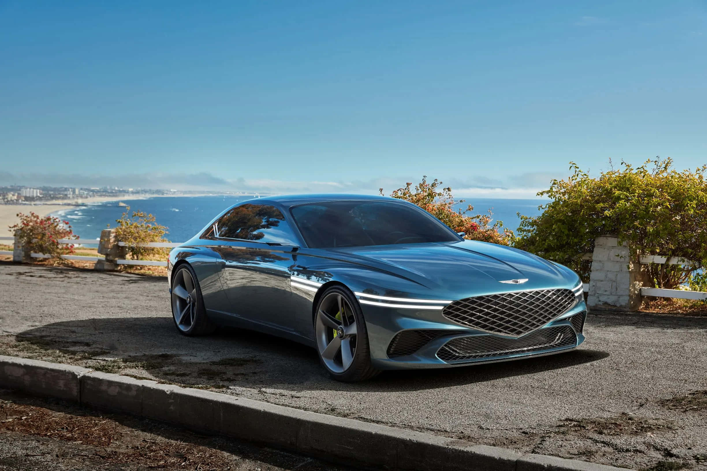 Genesis X Concept 桌布 壁紙 — 一架時尚金屬藍色跑車停泊在沿海公路上，俯瞰陽光普照的海灘和海洋。