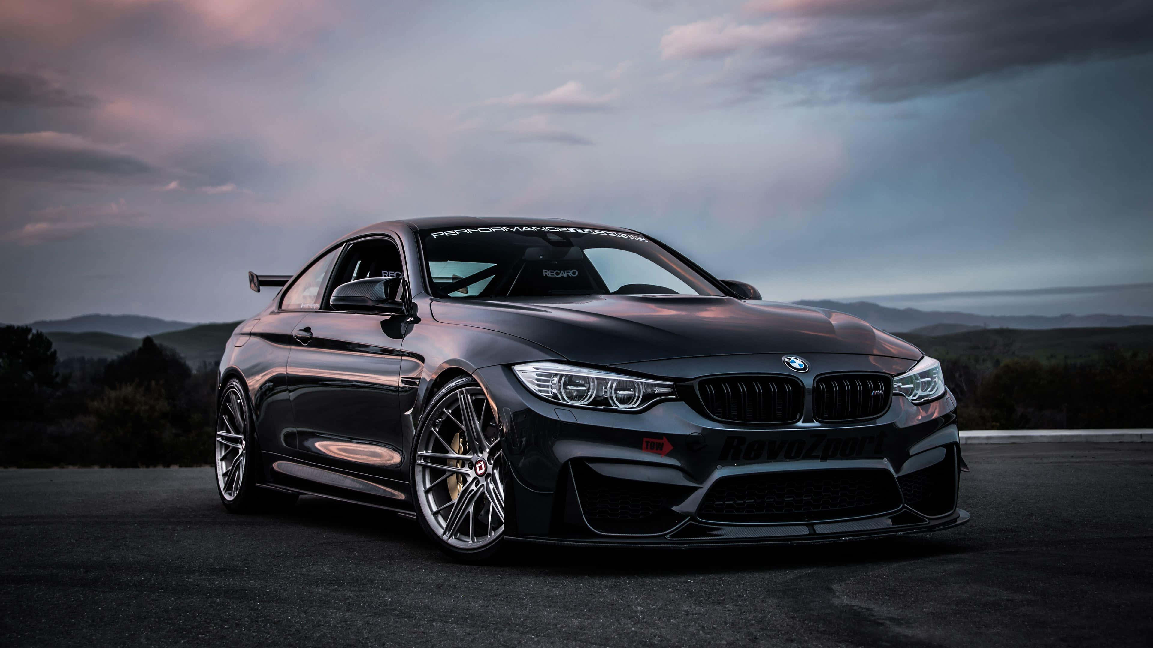 4K BMW 壁紙 桌布 壁紙 — 一架時尚黑色BMW M4雙門轎跑車，配備定制輪圈和後擾流板，停泊在黃昏時的瀝青路上，背景有山巒。