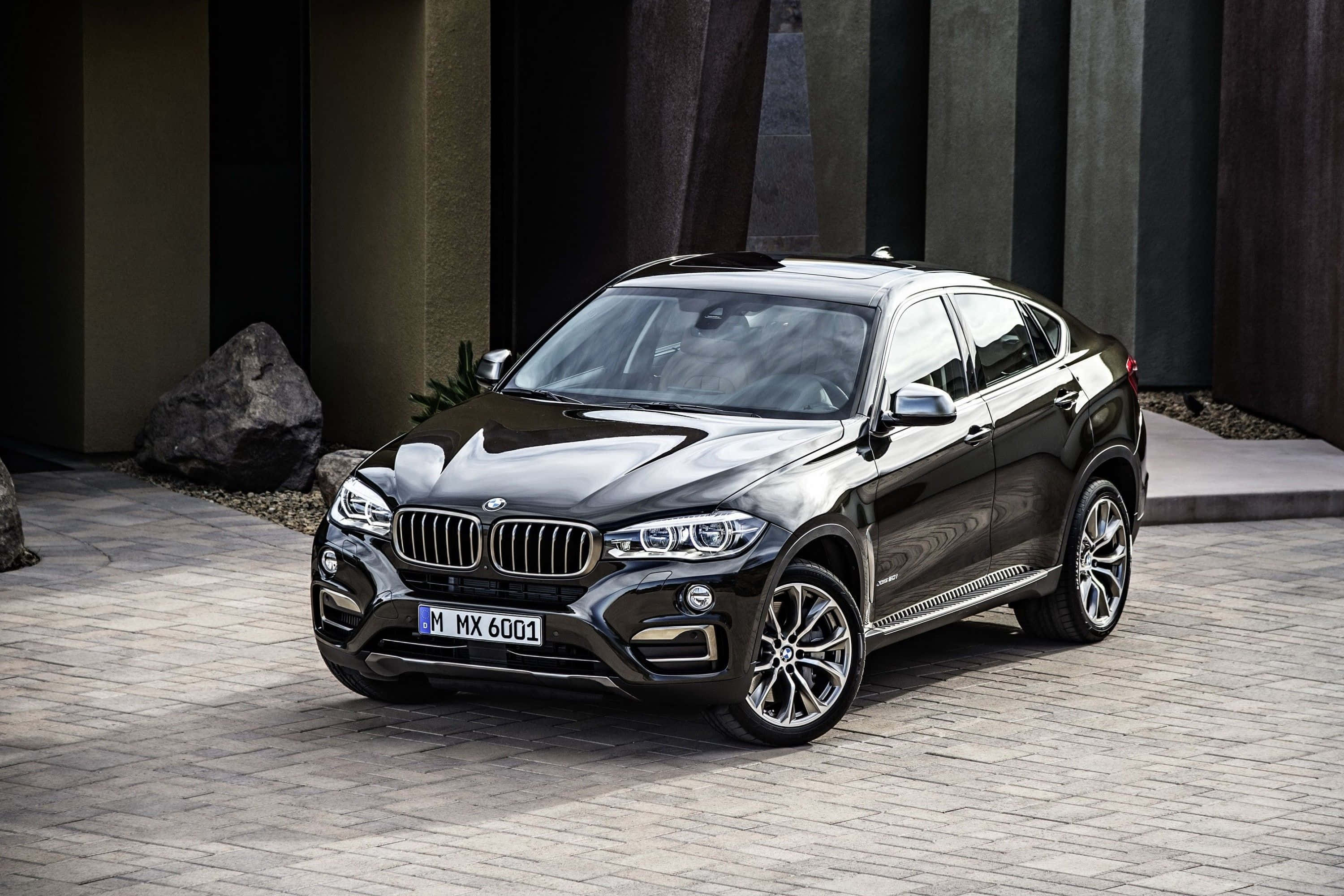Bmw X6 桌布 壁紙 — 一架時尚黑色BMW X6 M停泊在石砌車道上，旁邊是現代建築和大石頭。