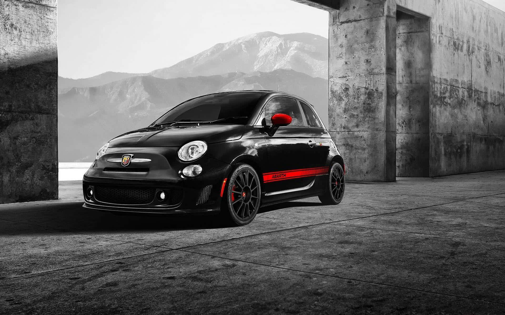 Abarth 桌布 壁紙 — 一架時尚黑色Fiat 500 Abarth，帶有紅色點綴，停泊在混凝土建築物內，背景係山巒。