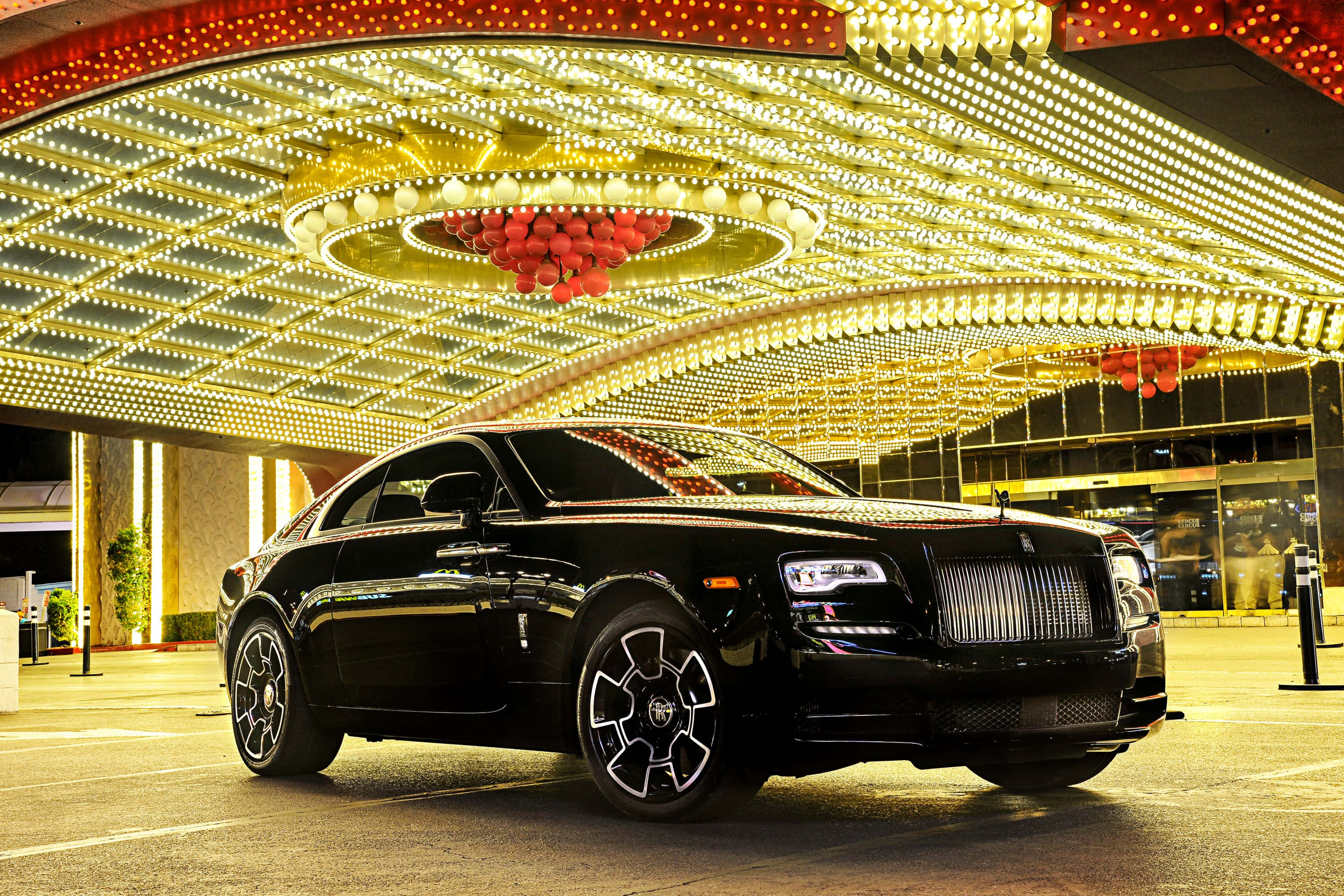Rolls Royce 桌布 壁紙 — 一架時尚黑色勞斯萊斯停泊在豪華酒店入口處耀眼金色燈光天篷下。