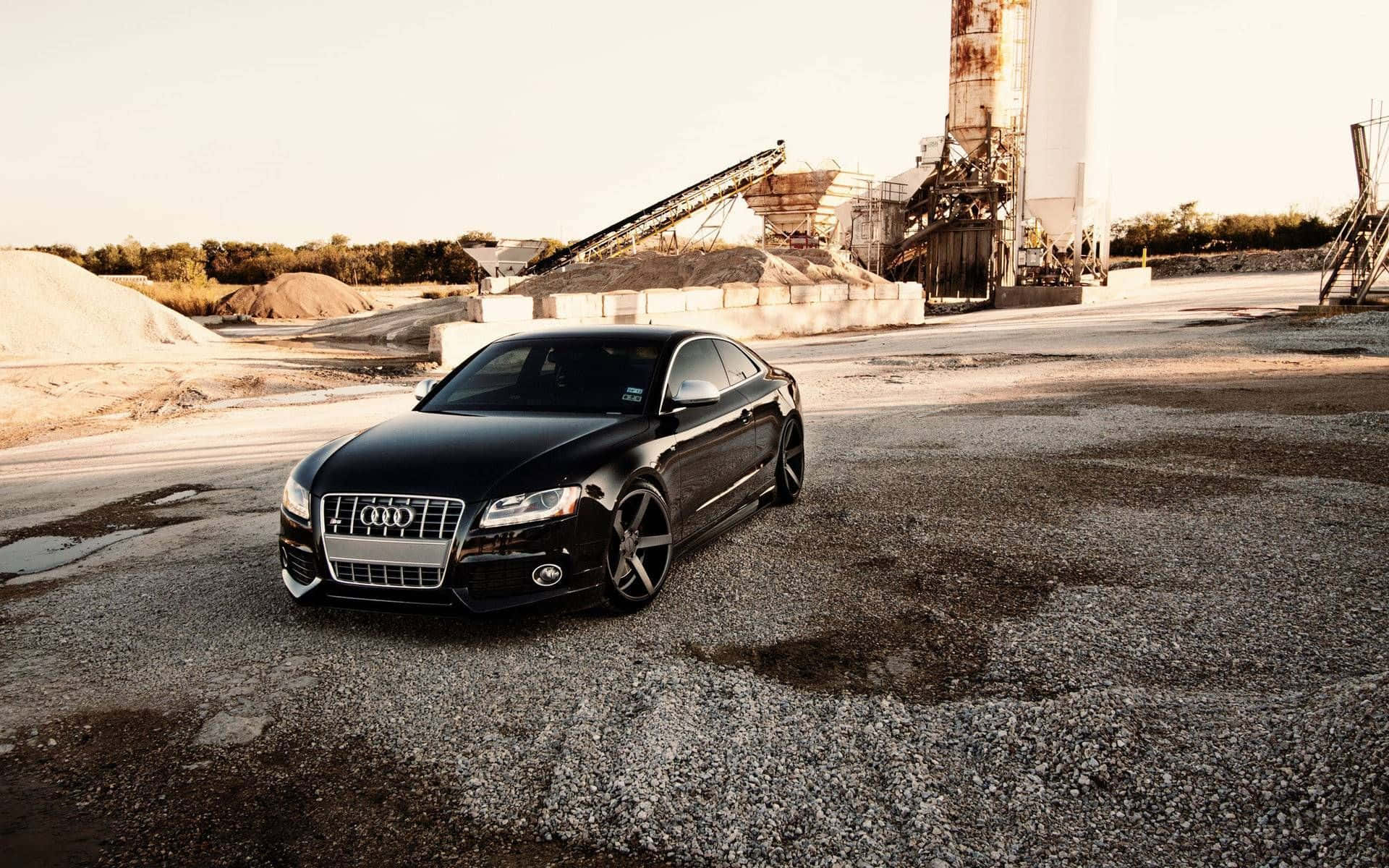 Audi S5 桌布 壁紙 — 一架時尚黑色奧迪房車停泊在工業採石場的碎石上，正值黃金時刻。