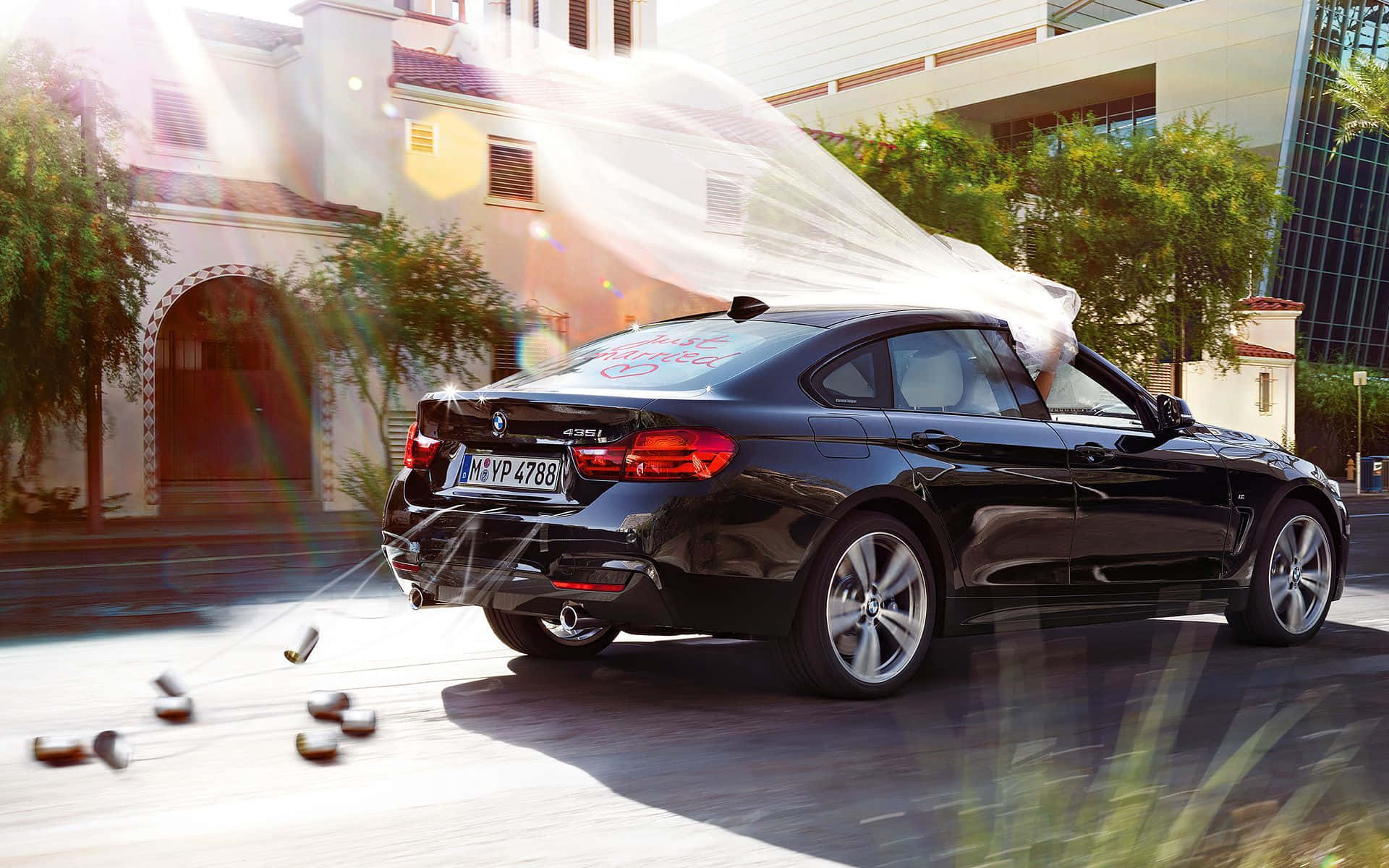 Bmw 4 Series 桌布 壁紙 — 一架時尚黑色寶馬房車在陽光明媚的城市街道上飛馳，散落香檳瓶並噴出氣泡。