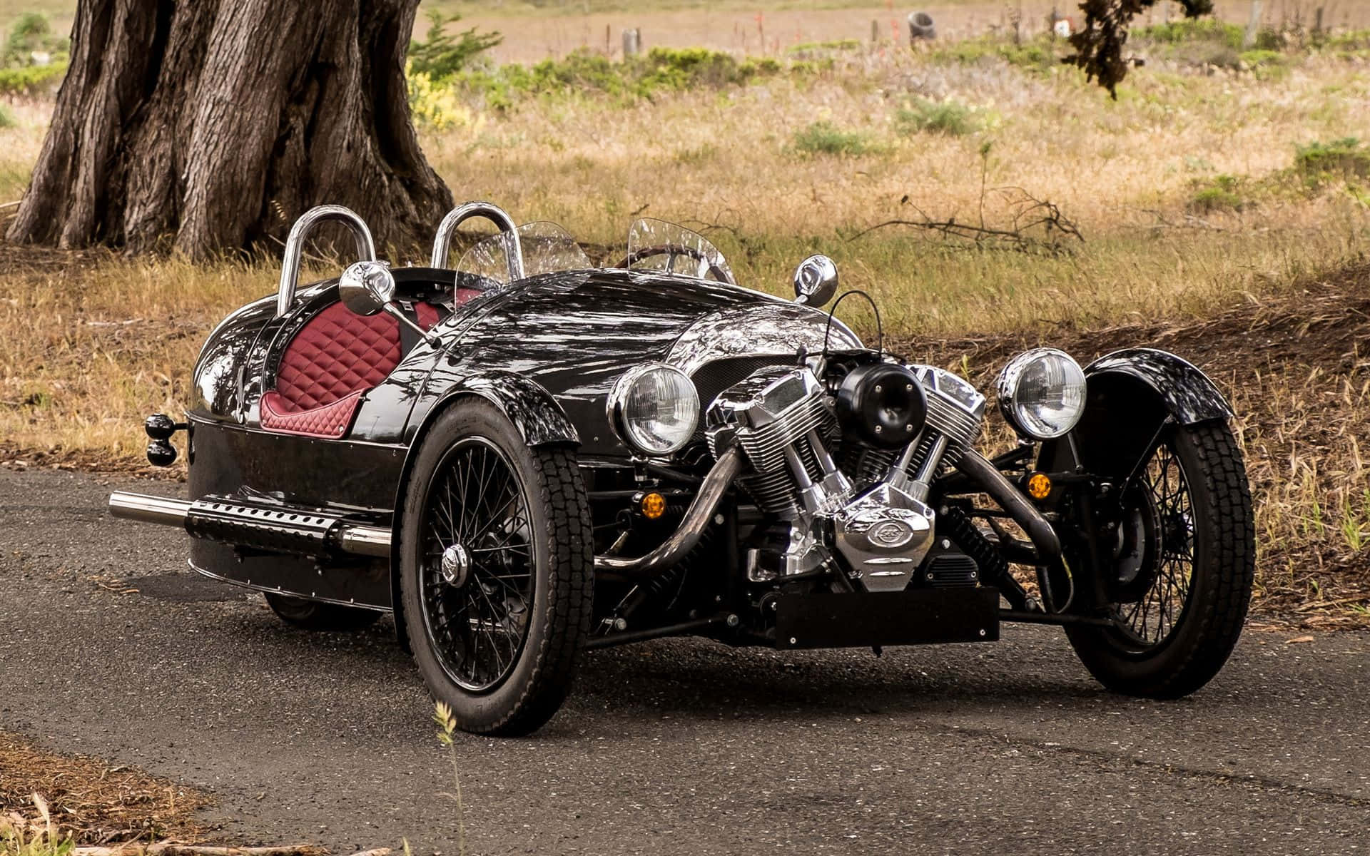 Morgan 桌布 壁紙 — 一架時尚黑色復古電單車，配紅色菱格座椅，停泊在乾草地大樹旁的碎石路上。