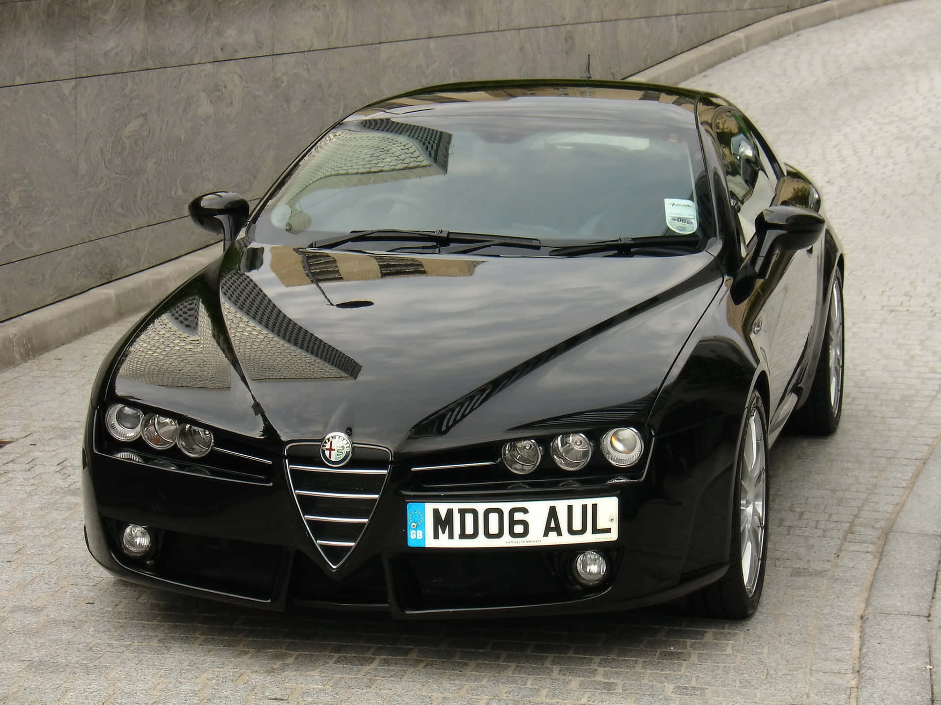 Alfa Romeo Brera 桌布 壁紙 — 一架時尚黑色愛快羅密歐跑車停泊在石牆旁邊的鵝卵石街道上。