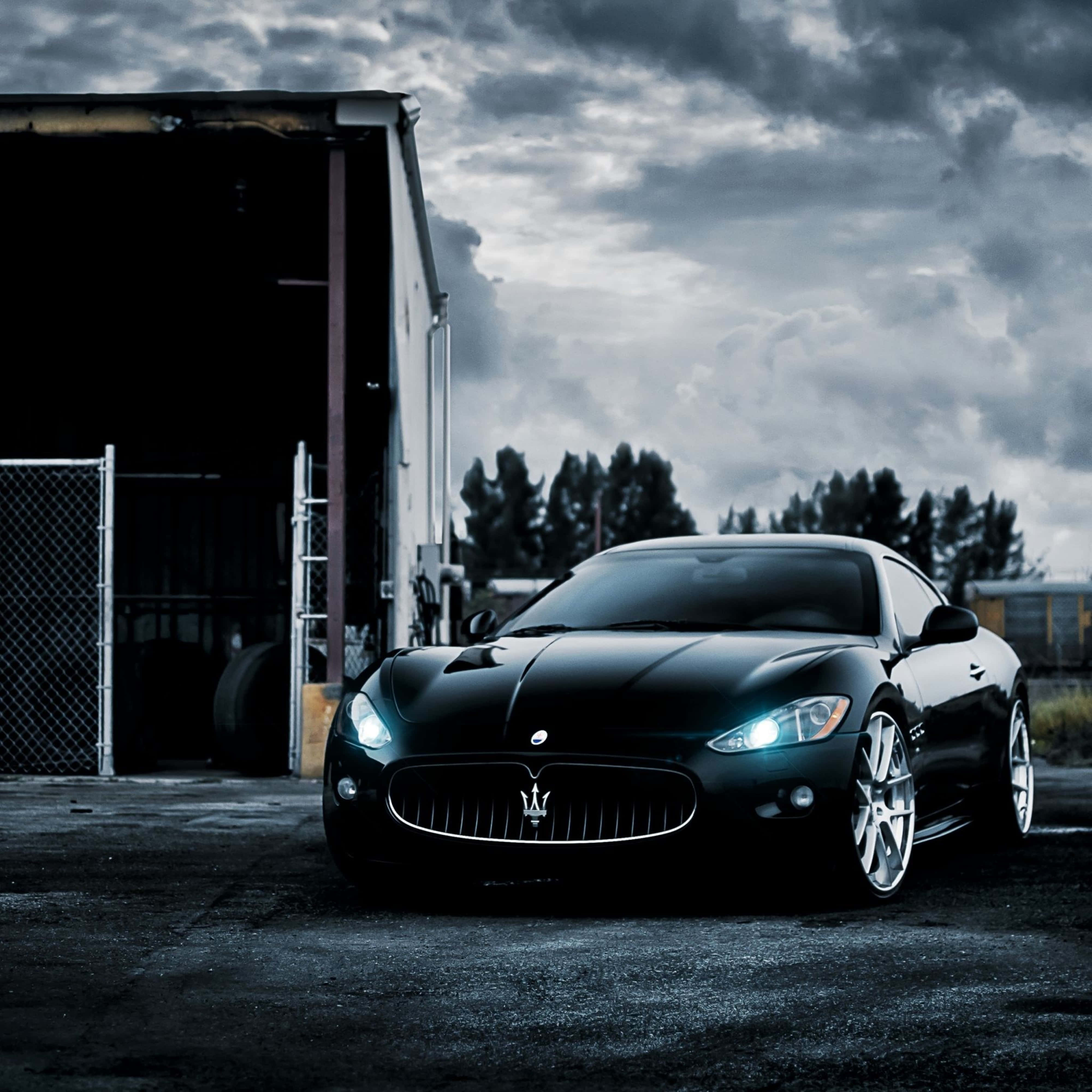 Maserati Aesthetic 4K 壁紙 — 一架時尚黑色瑪莎拉蒂跑車在倉庫旁邊的戲劇性暴風雲下閃閃發光。