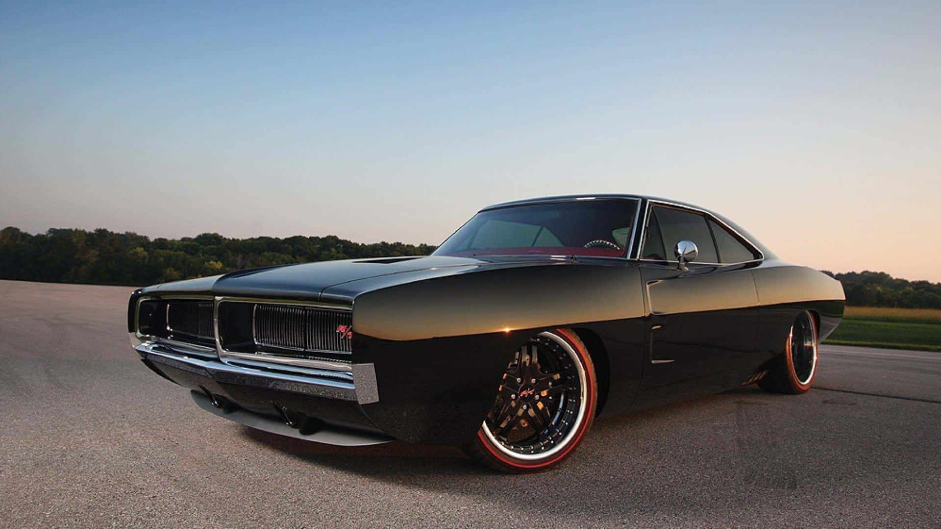Dodge Charger 桌布 壁紙 — 一架時尚黑色經典肌肉車，配紅色輪圈，在日落光線下於開闊道路上閃閃發光。