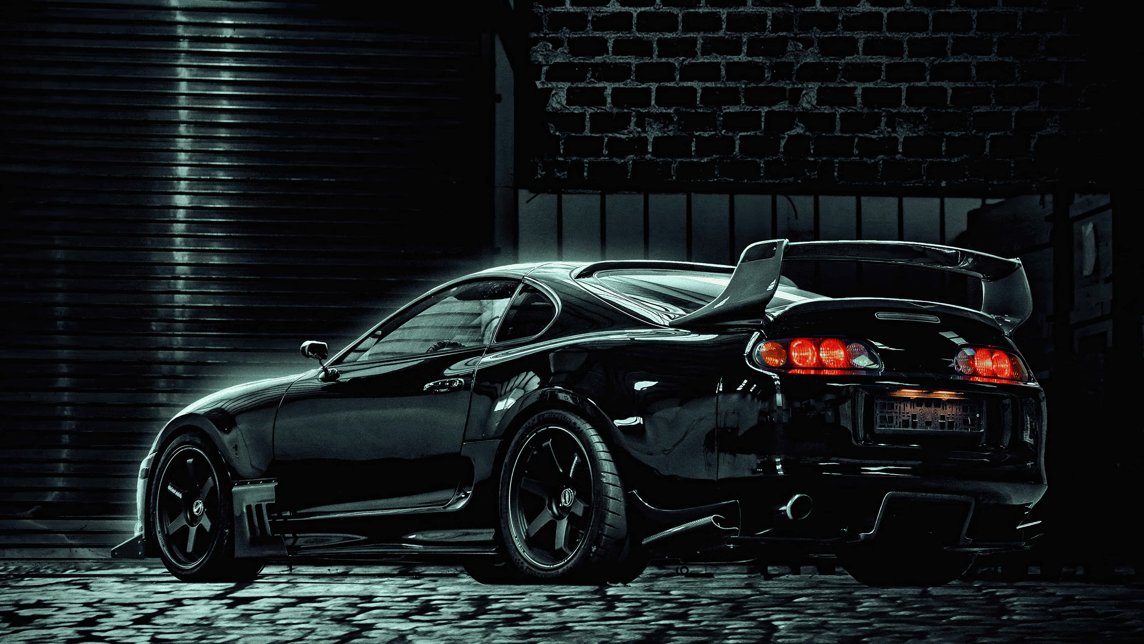 Supra 桌布 壁紙 — 一架時尚黑色跑車，紅色尾燈閃爍，停泊在鵝卵石路上，背景是磚牆，位於燈光昏暗的城市小巷中。