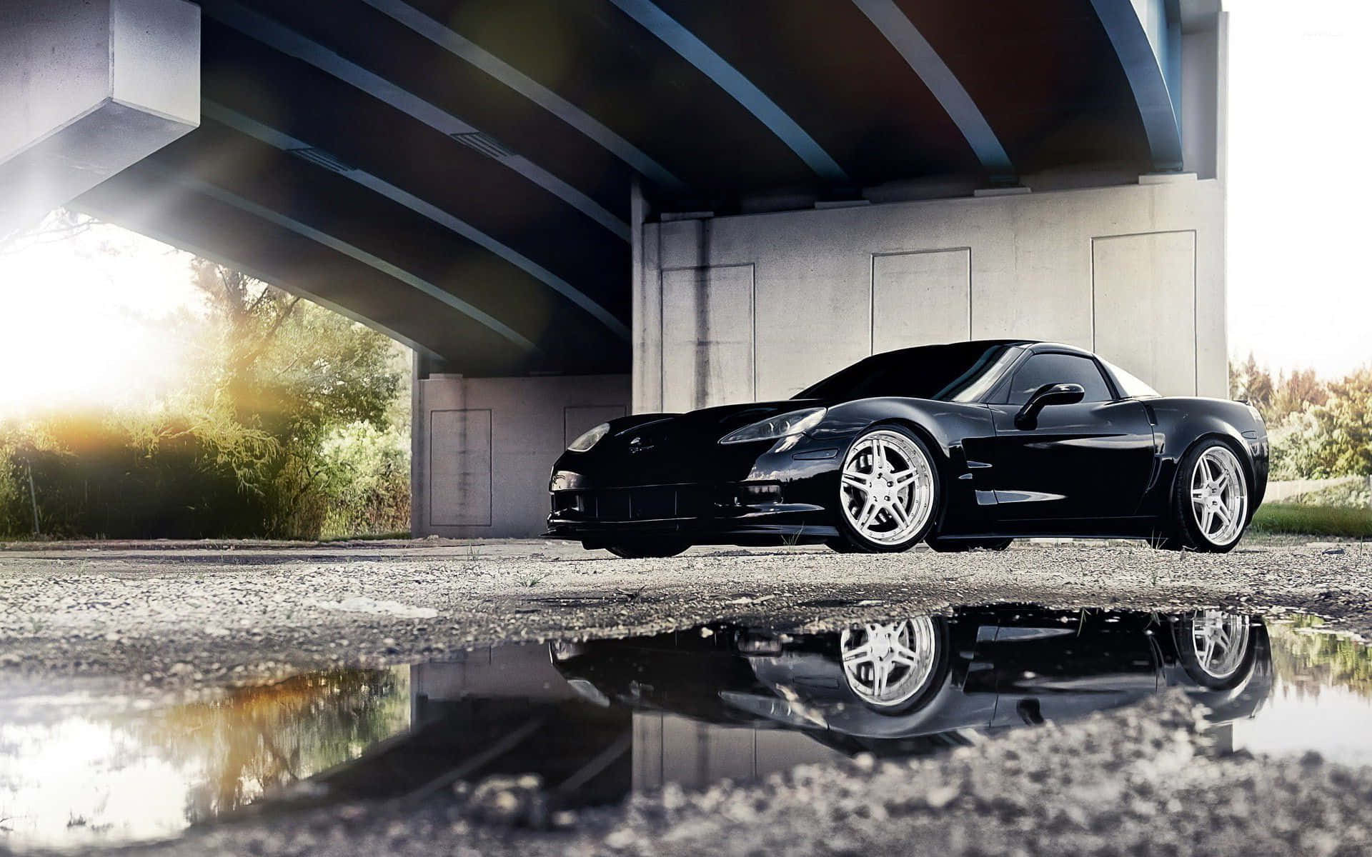 Chevrolet Corvette Z06 桌布 壁紙 — 一架時尚黑色跑車倒映在混凝土天橋下的水坑中，金色陽光穿透而過。