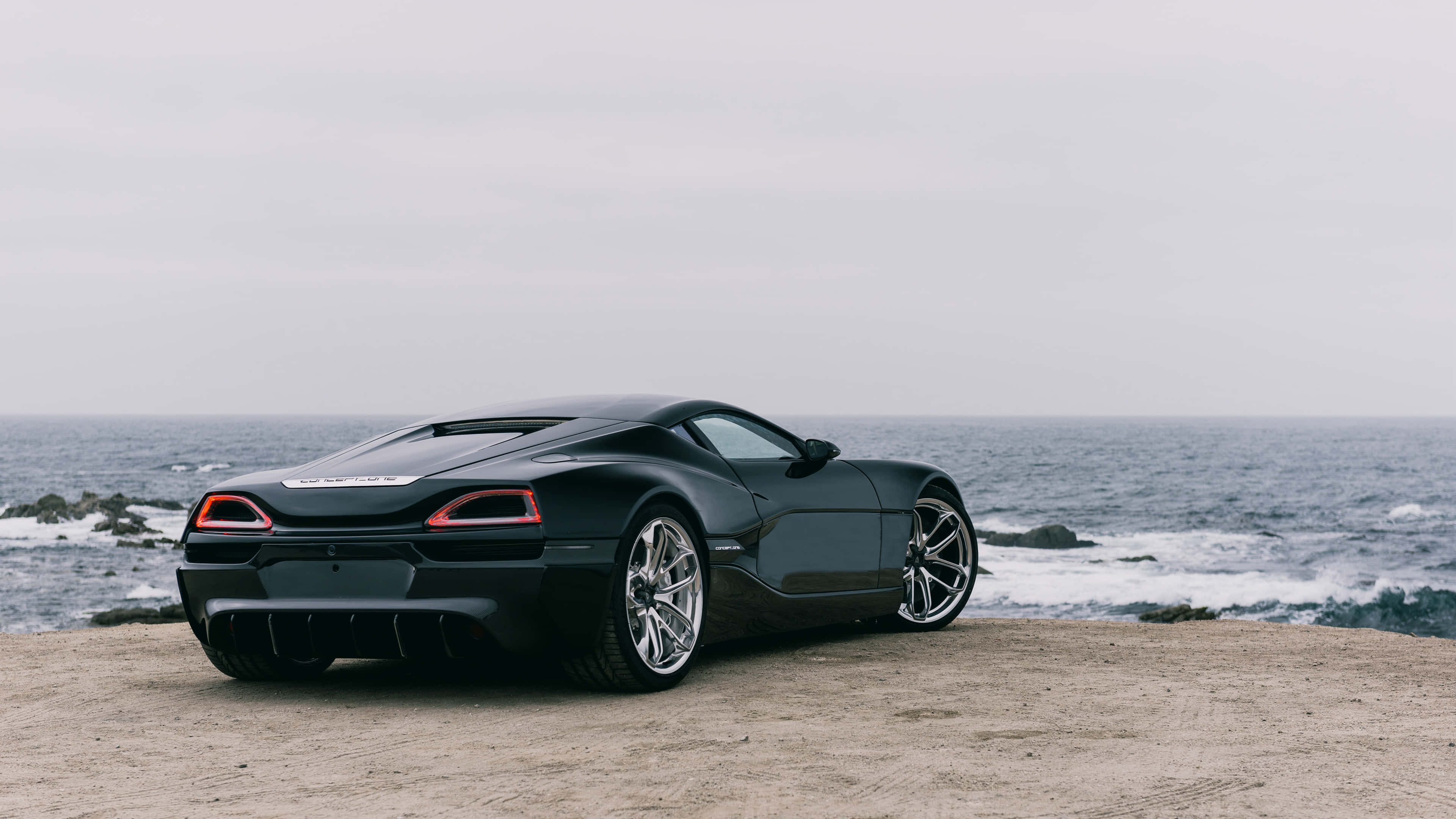 Rimac 桌布 壁紙 — 一架時尚黑色跑車停泊在崎嶇懸崖上，俯瞰著陰天下的暴風雨海洋。