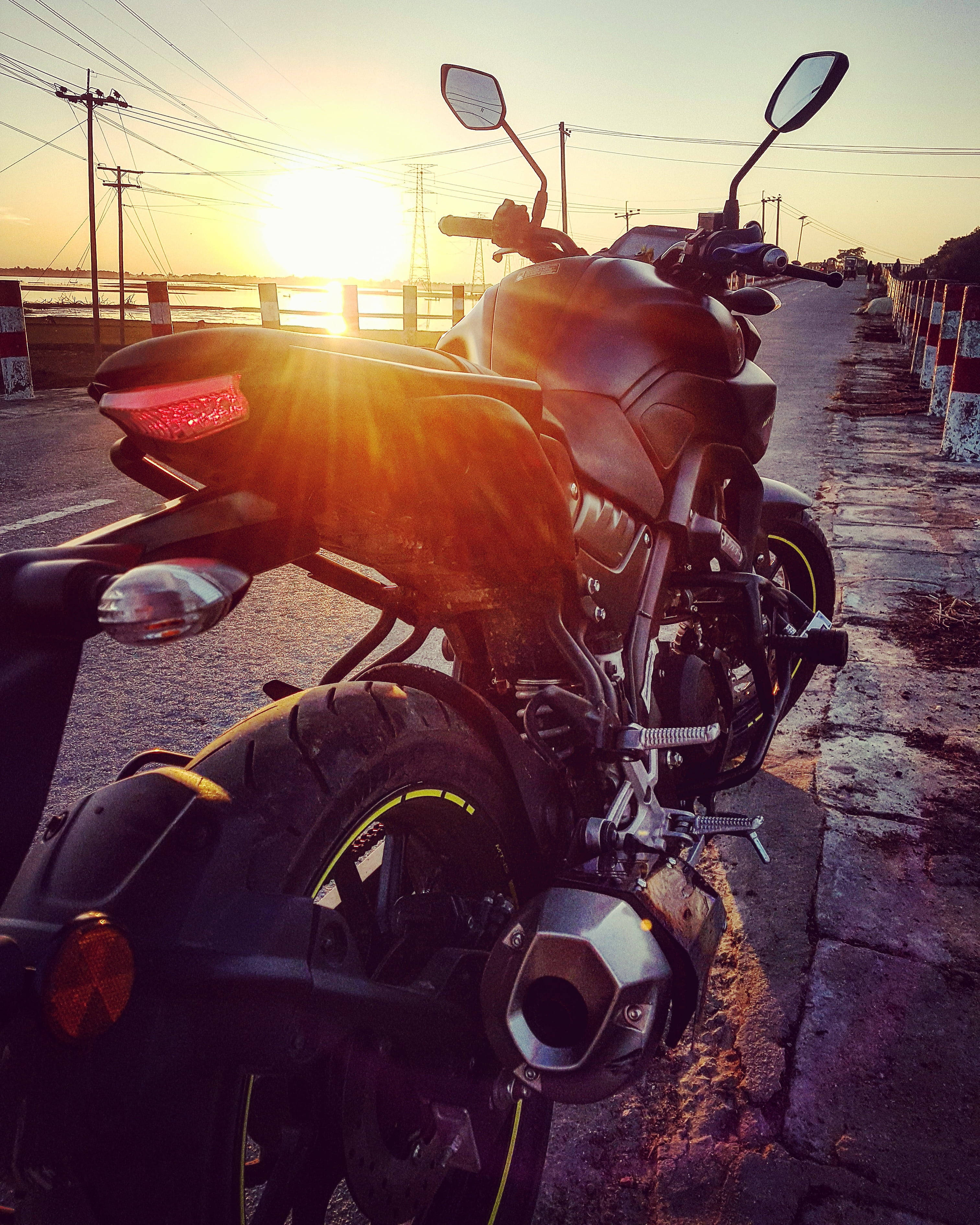 yamaha mt 15 桌布 壁紙 — 一架時尚黑色電單車停泊在日落時分的路邊，背後有金色光芒綻放。