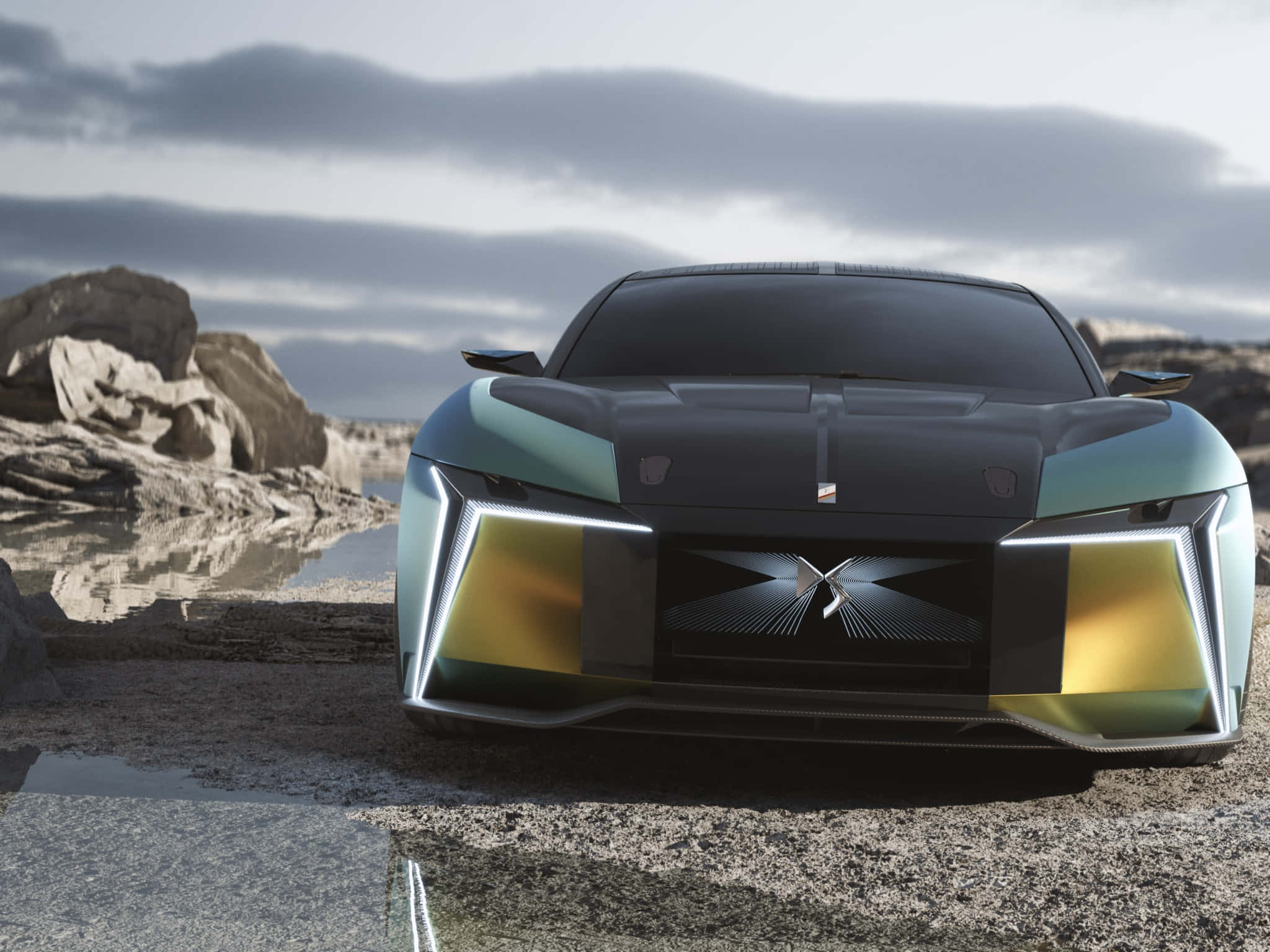 Ds Automobiles 桌布 壁紙 — 一架未來感十足的青綠色和金色跑車，配備發光車頭燈，停泊在岩石海岸上，天空多雲。