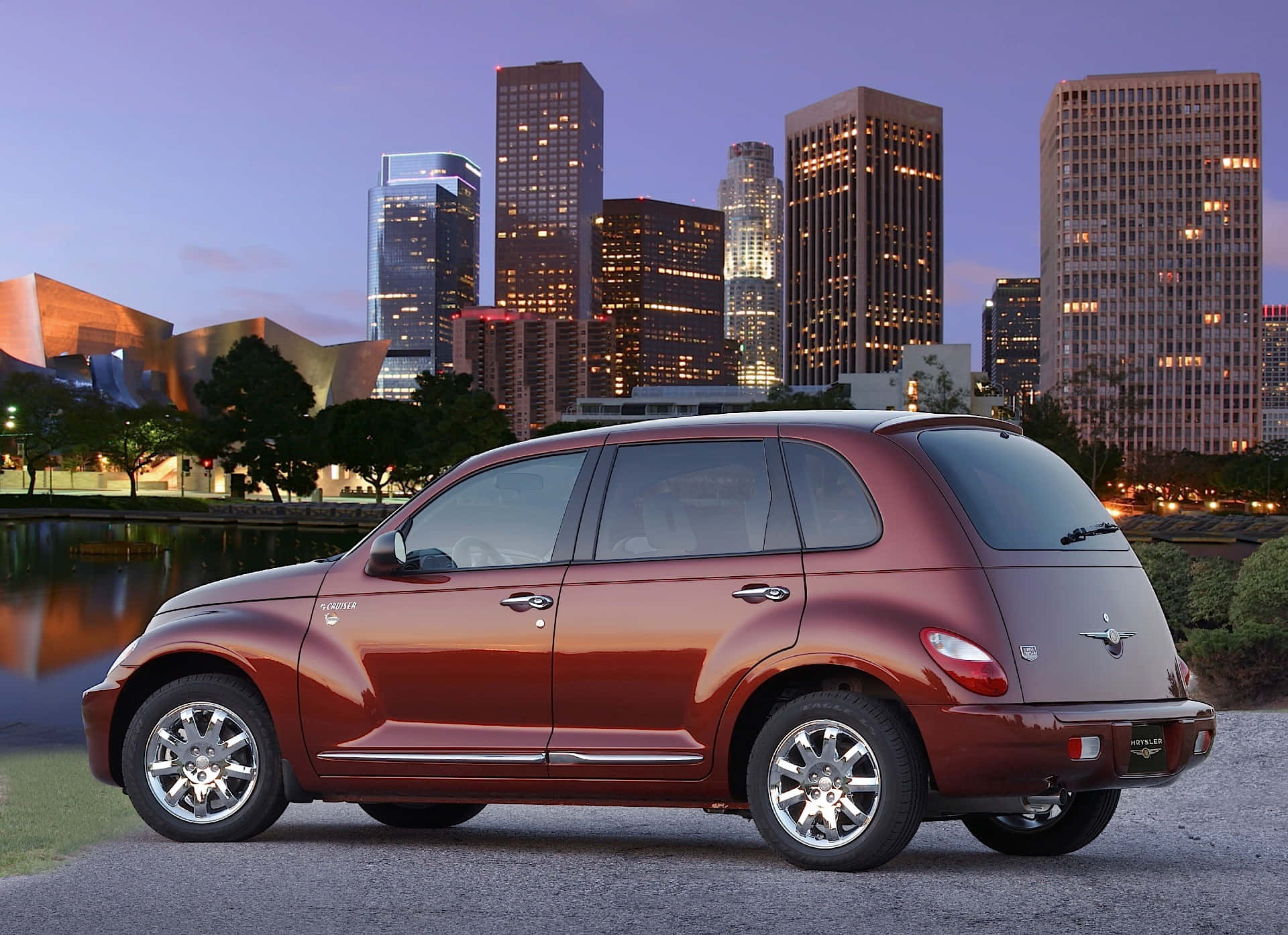 Chrysler Pt Cruiser 桌布 壁紙 — 一架栗色PT Cruiser停泊在水邊，背後是黃昏時分燈火通明的城市天際線。