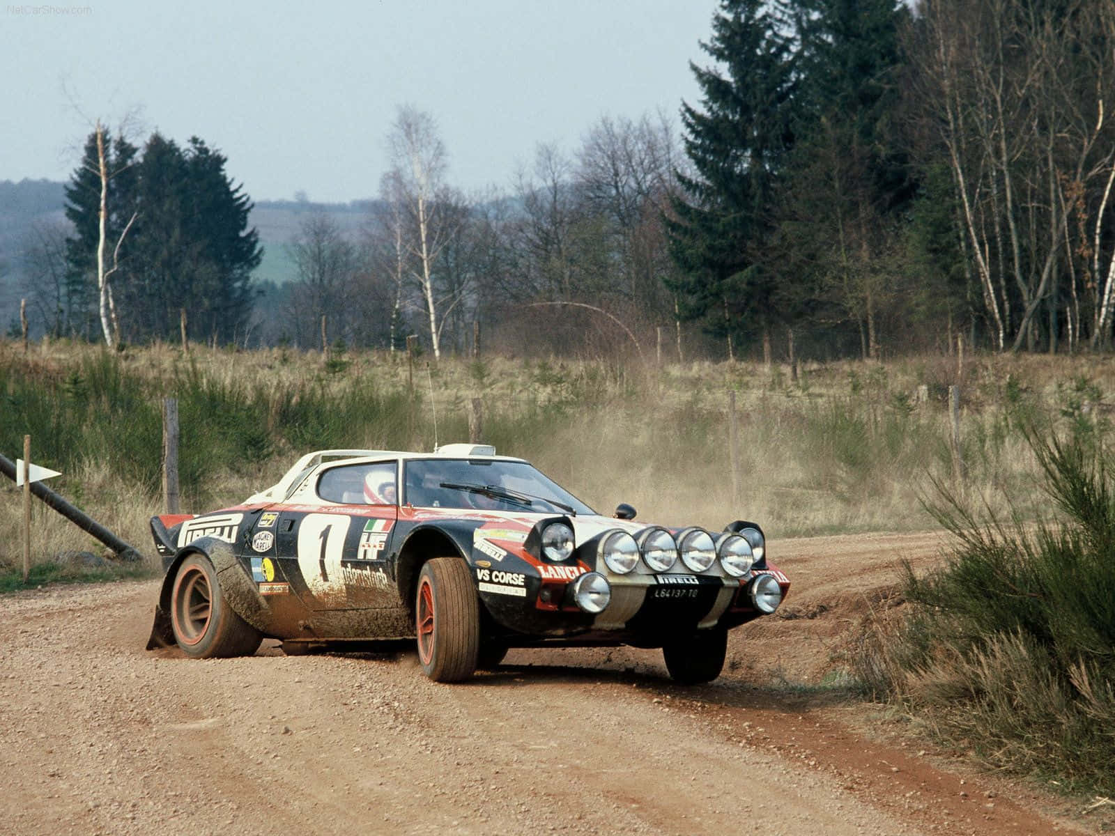 Lancia 桌布 壁紙 — 一架沾滿泥濘、配備多個車頭燈的藍旗亞 037 拉力賽車，在塵土飛揚的林間小徑上疾馳。