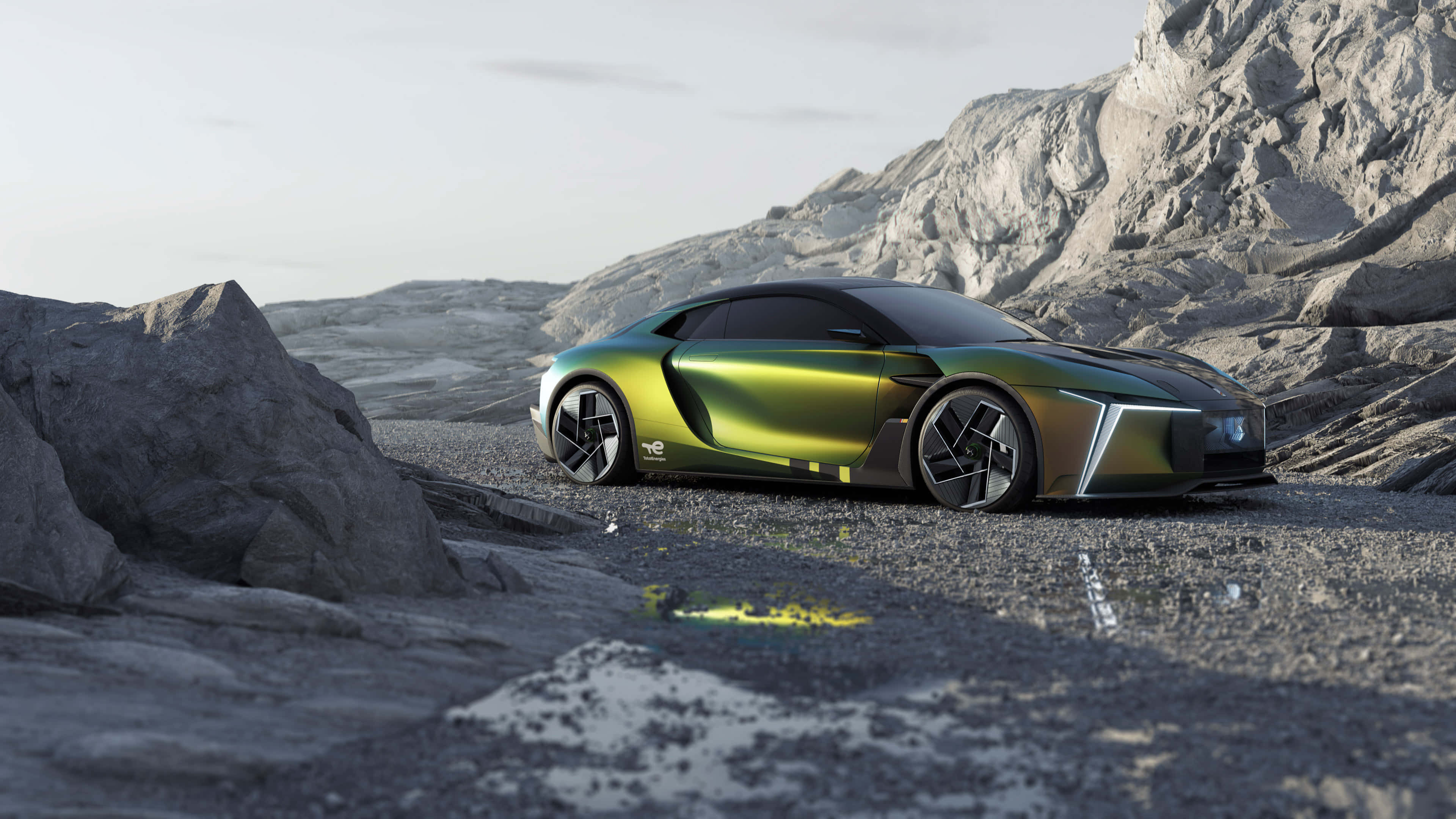 Ds Automobiles 桌布 壁紙 — 一架流線型未來感綠色跑車停泊在岩石地形上，背景是鋸齒狀山脈，天空蒼白。
