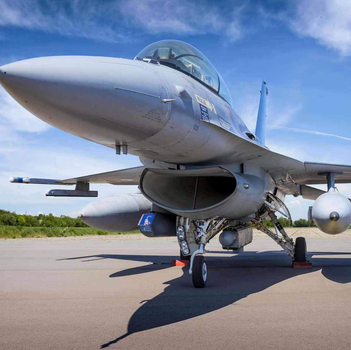 空軍 桌布 壁紙 — 一架流線型灰色戰鬥機搭載導彈，停在停機坪上，背景是晴朗藍天和零星白雲。