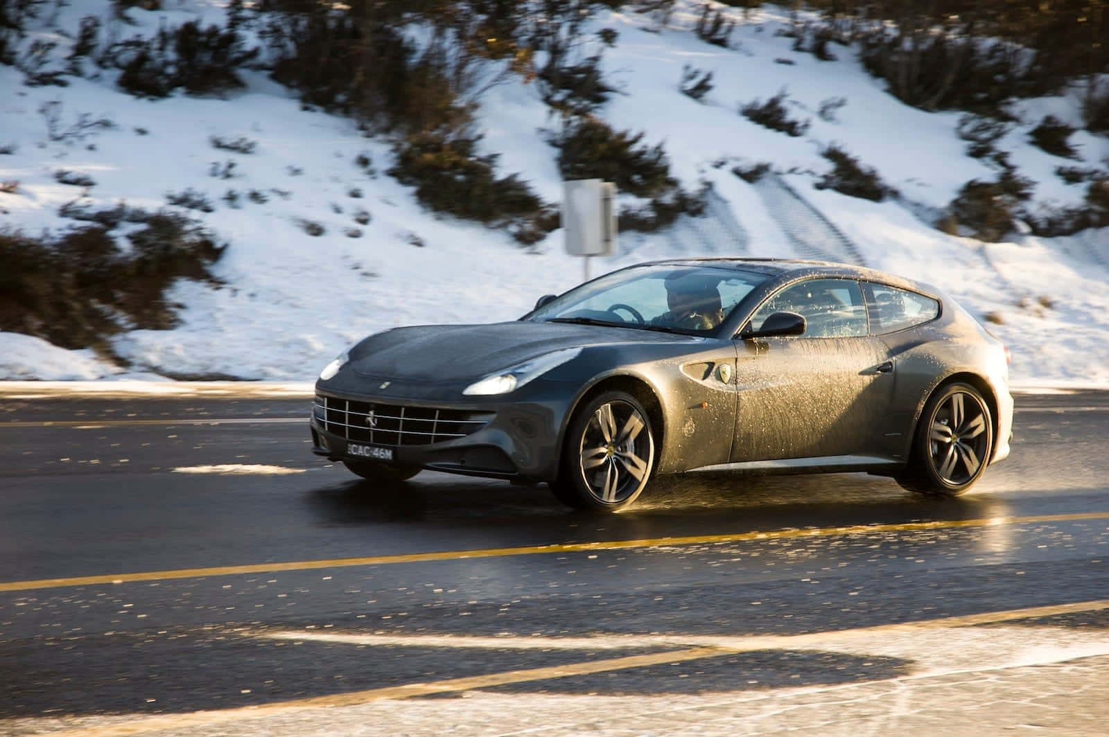 Ferrari Ff 桌布 壁紙 — 一架流線型灰色法拉利在白雪覆蓋的山路上行駛，背景是陽光普照的雪山丘陵。