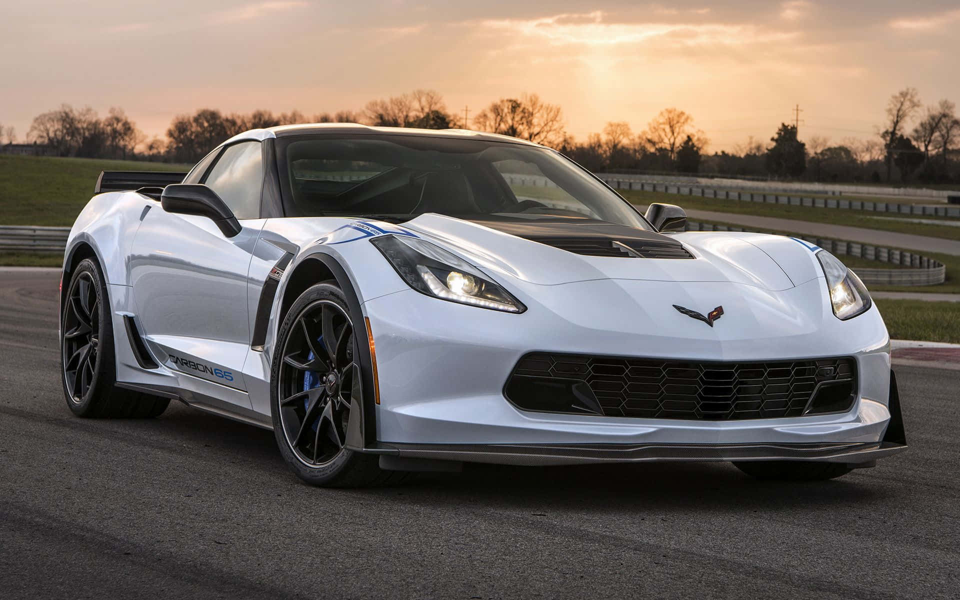 Chevrolet Corvette Z06 桌布 壁紙 — 一架流線型白色 Corvette C7.R 跑車在金色夕陽下、背景有光禿樹木的賽道上閃閃發光。