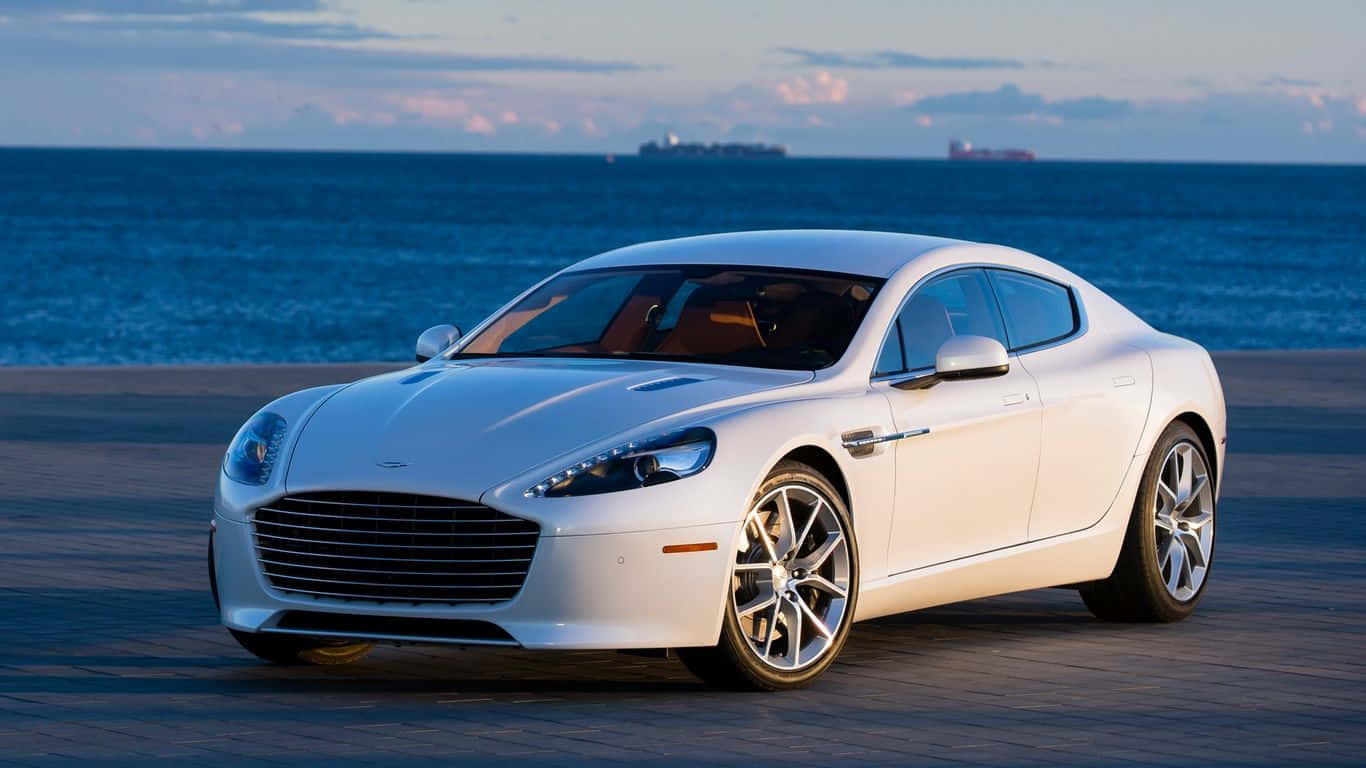 Aston Martin Rapide S 桌布 壁紙 — 一架流線型白色Aston Martin跑車停泊在海濱長廊，背景是日落時分的海洋和船隻。