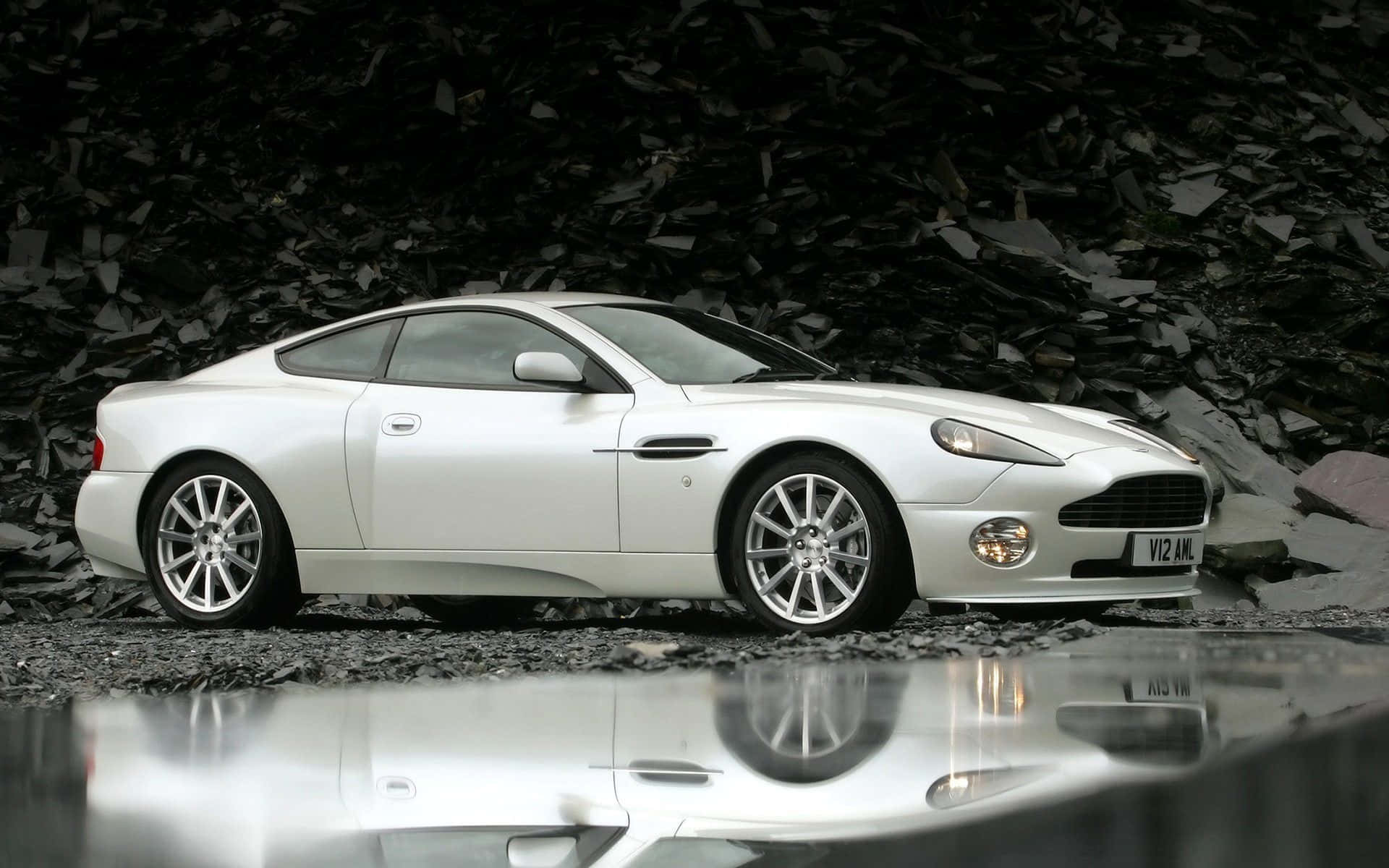 Aston Martin Vanquish 桌布 壁紙 — 一架流線型白色Aston Martin跑車在濕潤的礫石上反射，背景是黑暗的岩石。