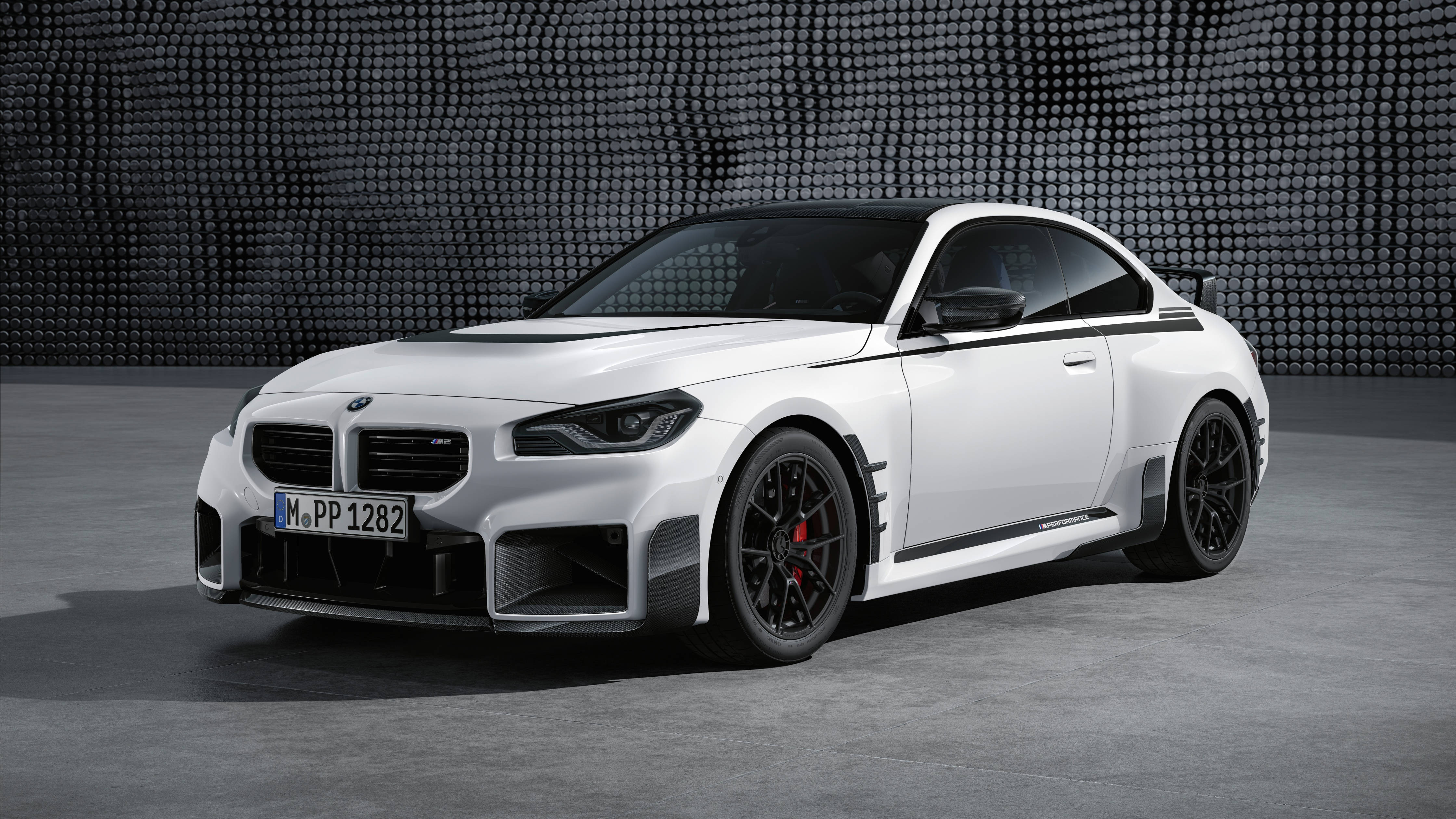 Bmw 桌布 壁紙 — 一架流線型白色BMW M2 Competition雙門轎跑車，帶有黑色飾件和紅色制動卡鉗，在紋理灰色牆壁前蓄勢待發。