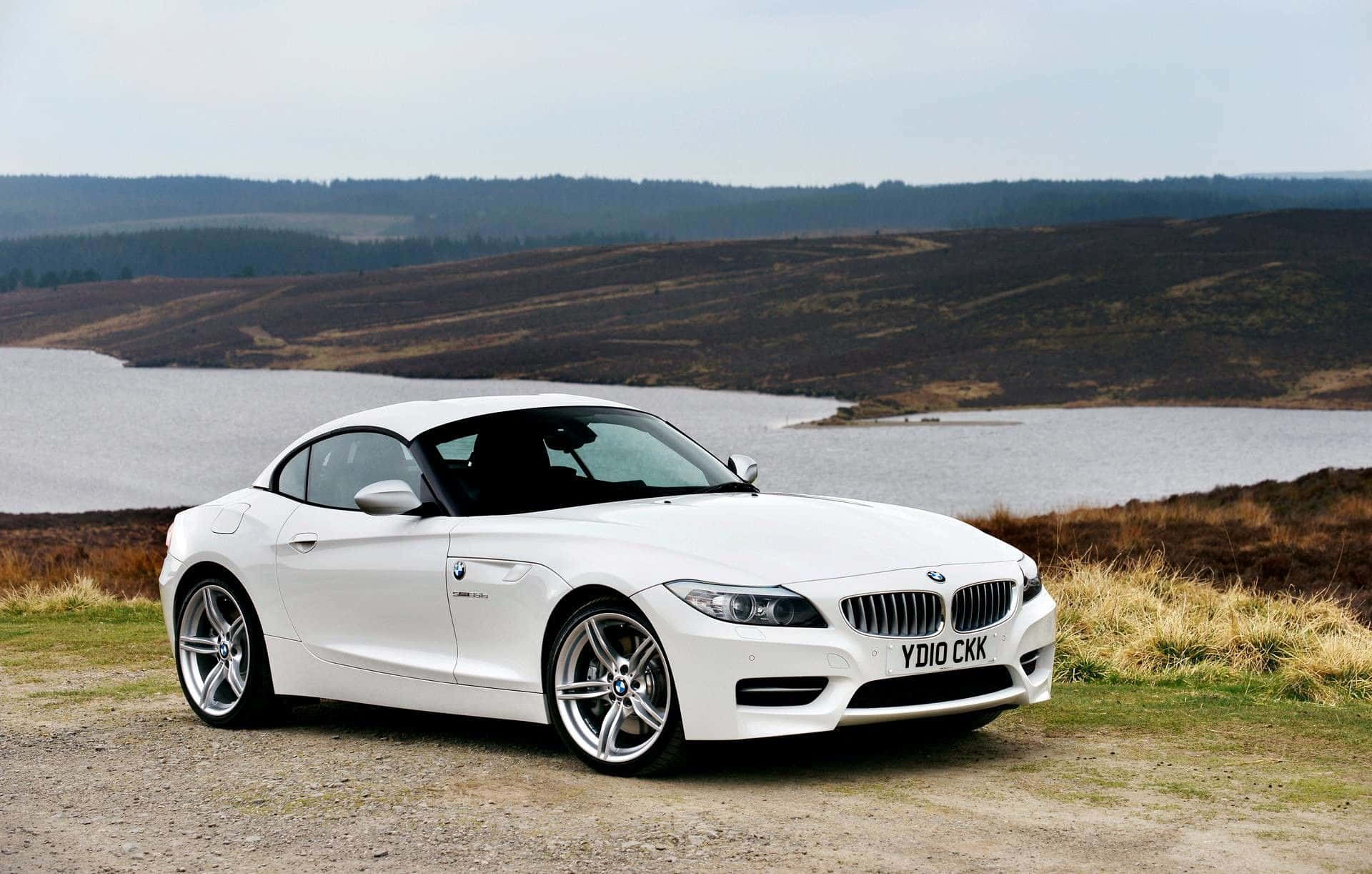 Bmw Z4 桌布 壁紙 — 一架流線型白色BMW Z4開篷跑車停泊在青草山坡上，俯瞰平靜湖泊，背景是起伏的荒野丘陵。