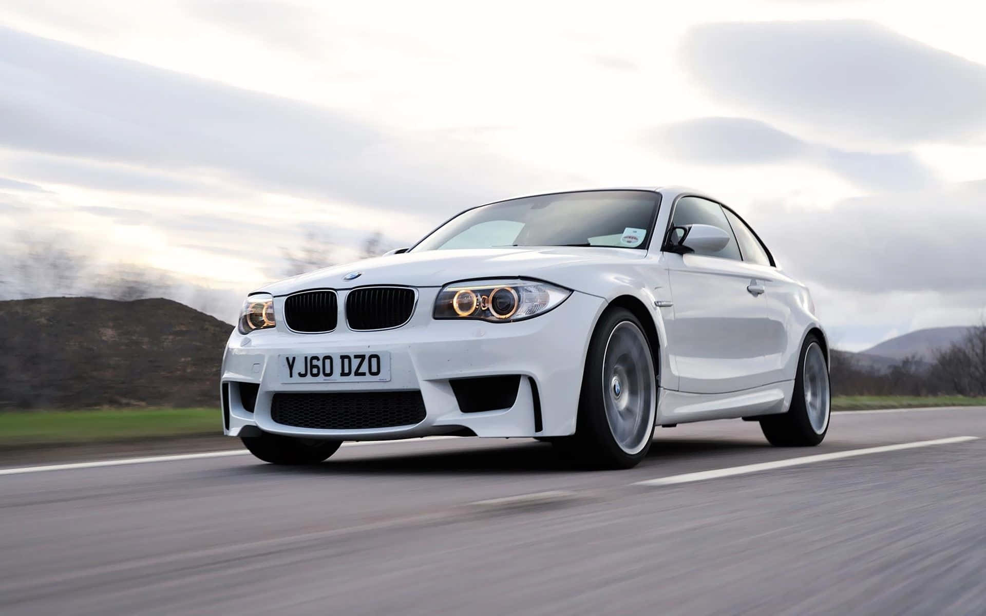 Bmw 1 Series 桌布 壁紙 — 一架流線型白色BMW跑車在陰天嘅鄉村道路上高速行駛，呈現動態模糊效果。