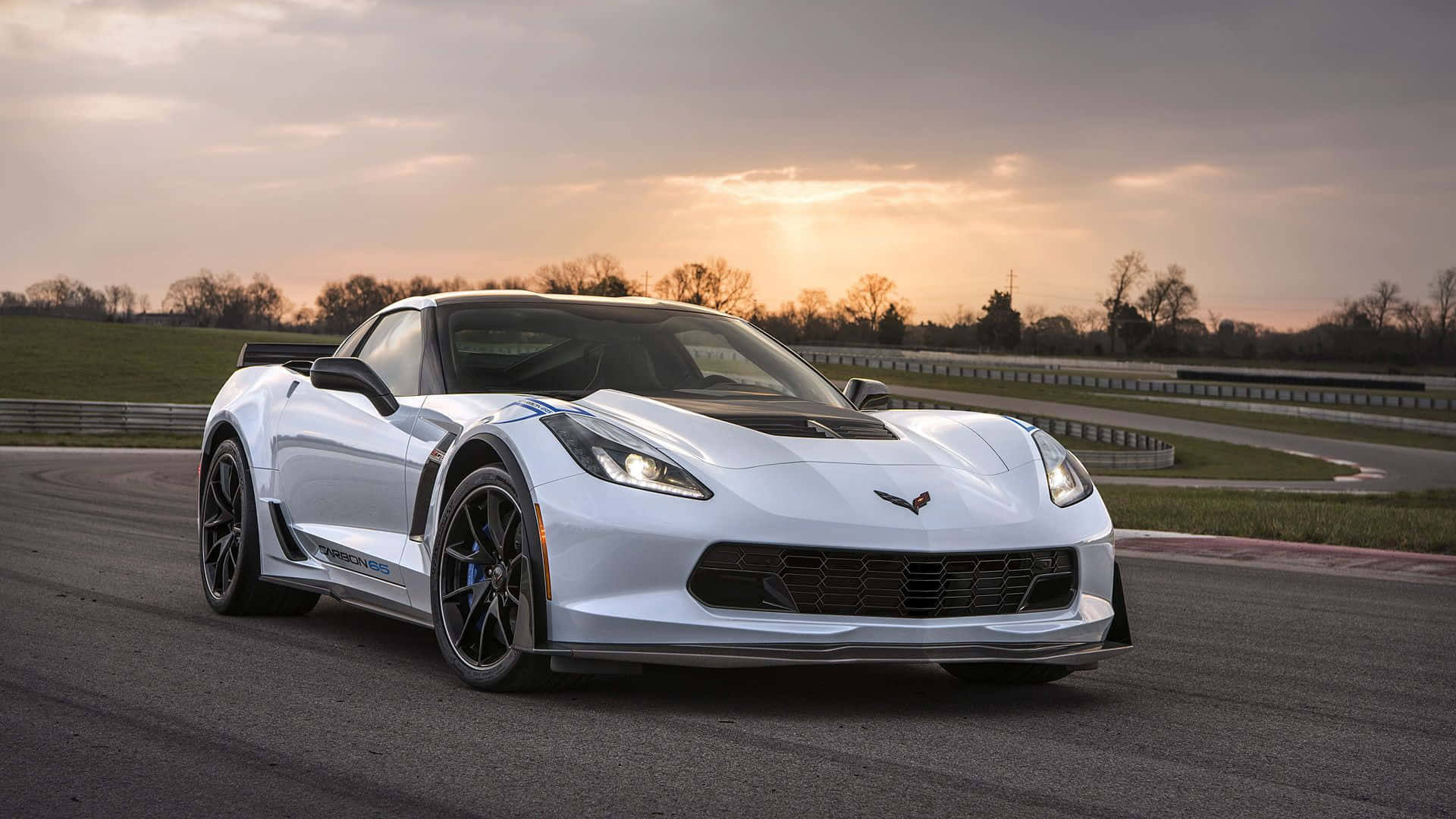 corvette 桌布 壁紙 — 一架流線型白色Corvette跑車在日落時分沿著蜿蜒的賽道滑行，溫暖的金色光芒投下長長的影子。