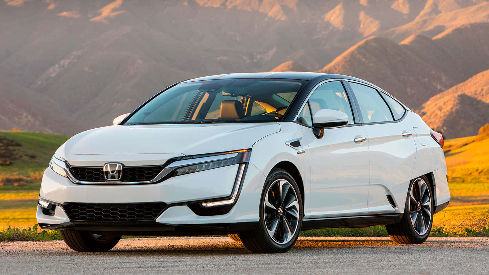 Honda Clarity 桌布 壁紙 — 一架流線型白色本田Clarity插電式混合動力轎車停泊在道路上，背景是陽光普照的起伏山丘和遠處的山脈。