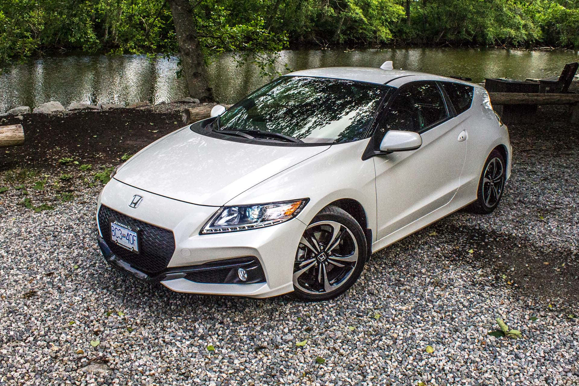 Honda Cr-z 桌布 壁紙 — 一架流線型白色本田S2000跑車停泊在碎石上，旁邊是平靜的河流，四周環繞著茂密的綠樹。