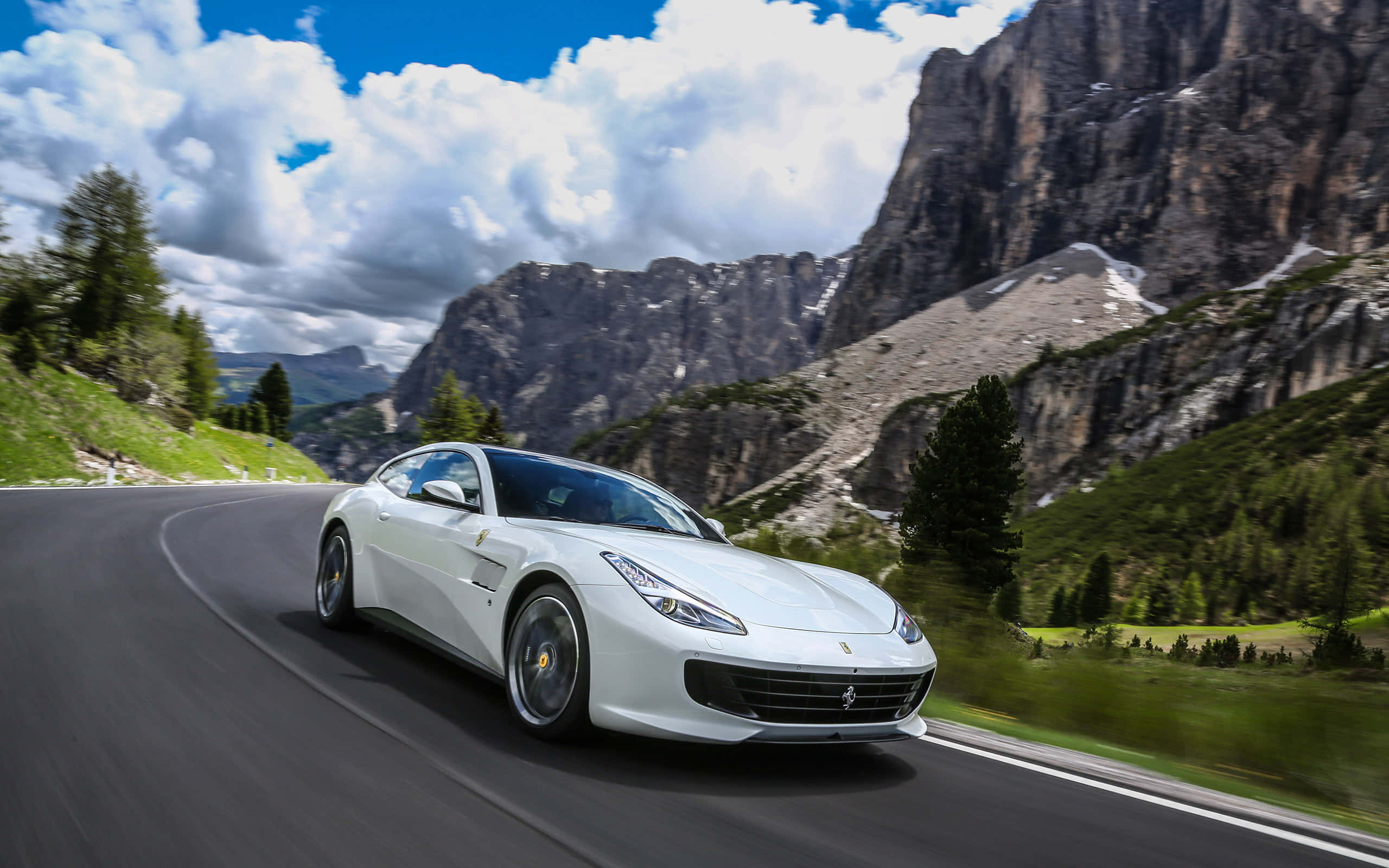 Ferrari Gtc4lusso 桌布 壁紙 — 一架流線型白色法拉利在戲劇性的雲層和崎嶇山峰下沿著蜿蜒的山路飛馳。