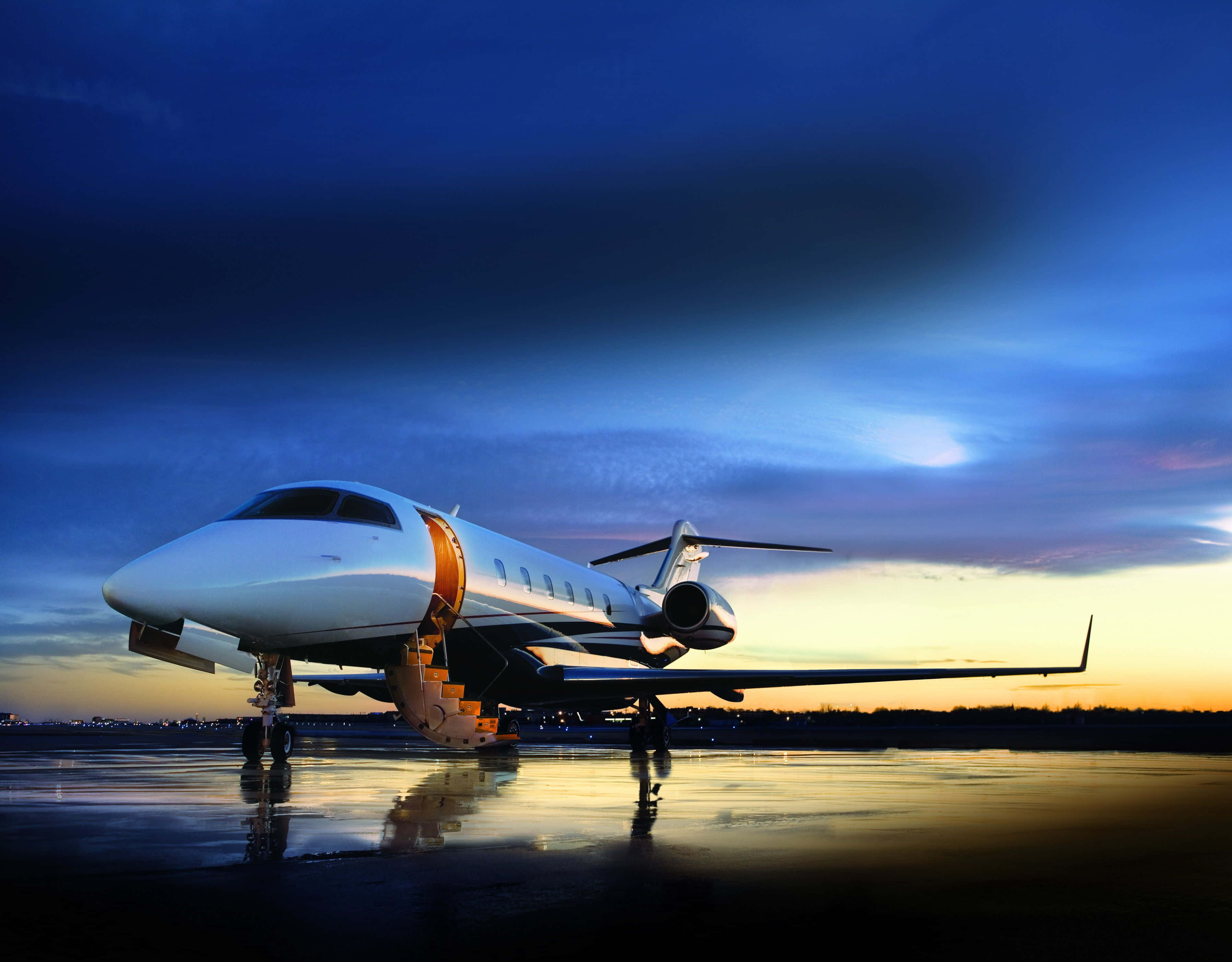 Jet 桌布 壁紙 — 一架流線型白色私人飛機在黃昏時停在濕滑的停機坪上，充滿活力的藍色和橙色天空倒映在水坑中。