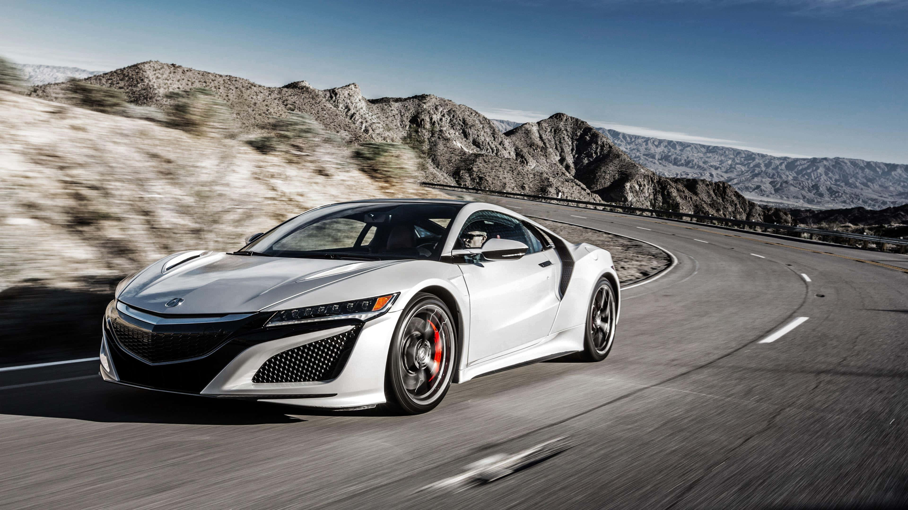 Acura Nsx 桌布 壁紙 — 一架流線型白色跑車在晴朗藍天下沿著蜿蜒的山路飛馳。