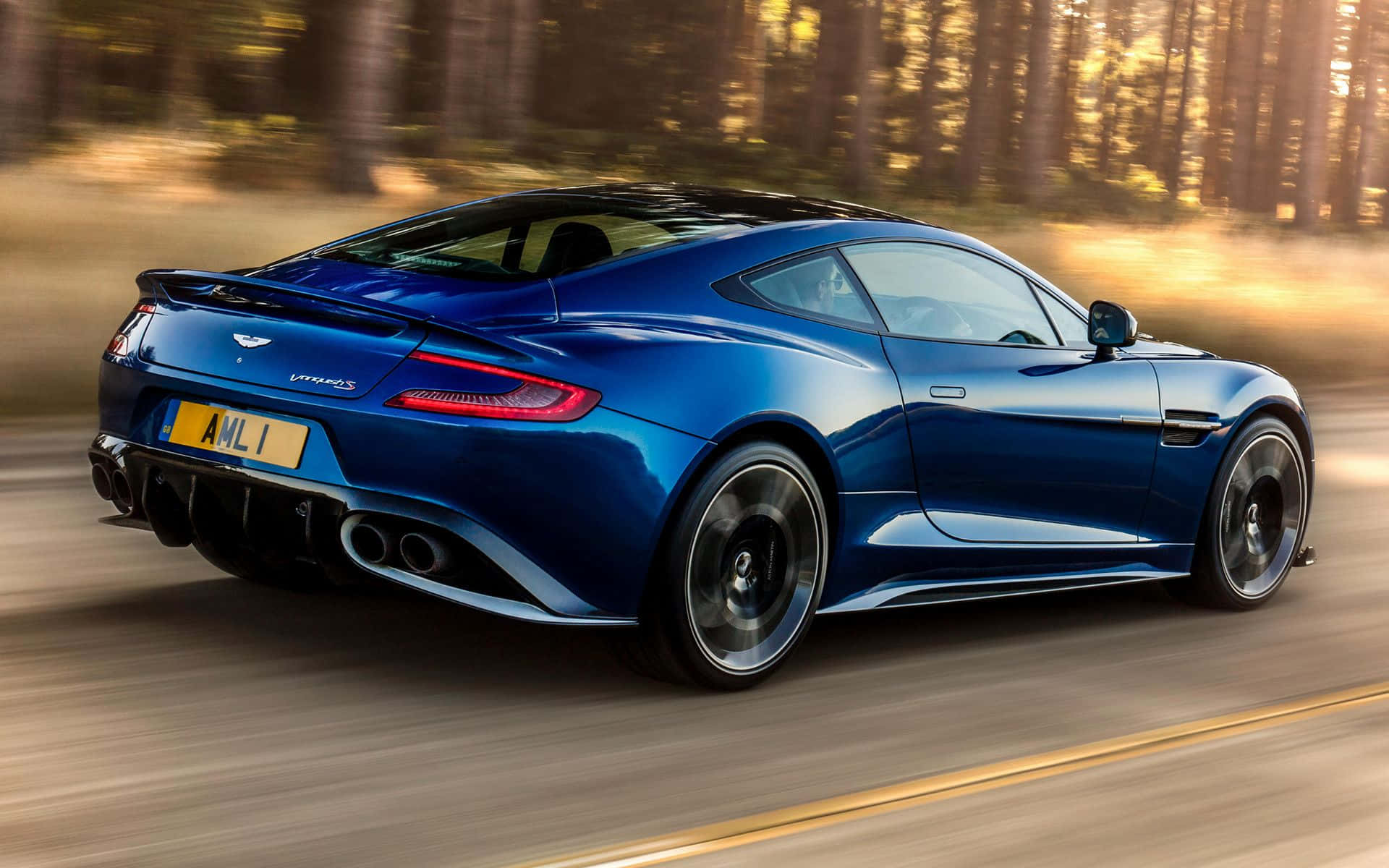 Aston Martin Vanquish 桌布 壁紙 — 一架流線型的藍色 Aston Martin Vanquish 在陽光明媚的森林中疾馳，動態模糊效果突顯其力量與優雅。