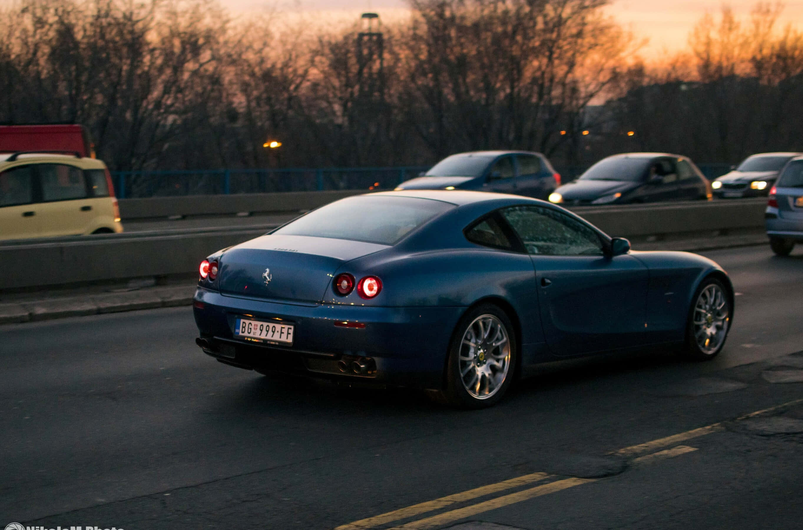 Ferrari 612 Scaglietti 桌布 壁紙 — 一架流線型的藍色法拉利612 Superamerica在日落時分於高速公路上行駛，尾燈閃爍，背景有光禿的樹木。