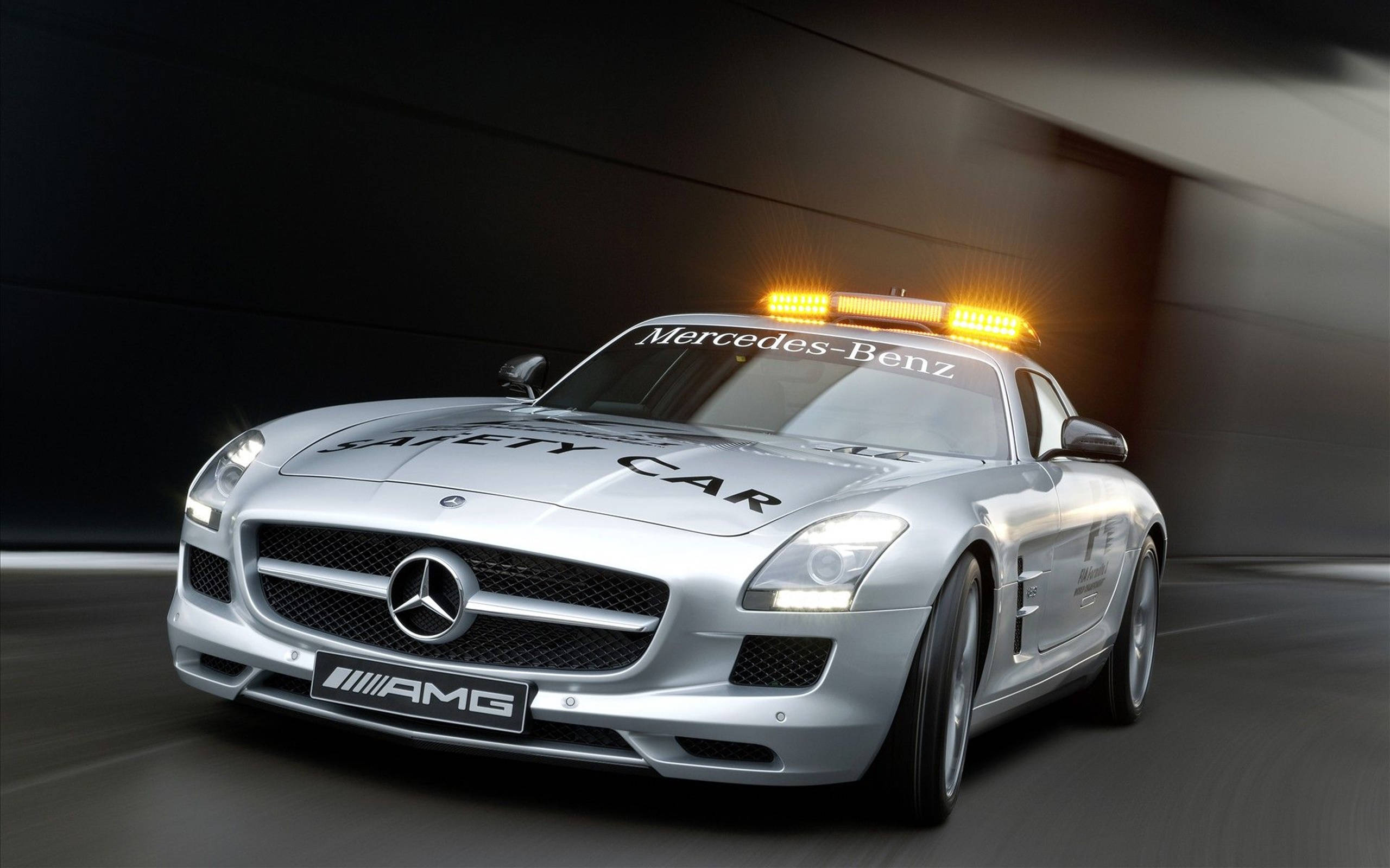 HD 桌布 壁紙 — 一架流線型的銀色 Mercedes-Benz SLS AMG 安全車在昏暗的隧道中疾馳，隧道頂部散發著琥珀色的燈光。