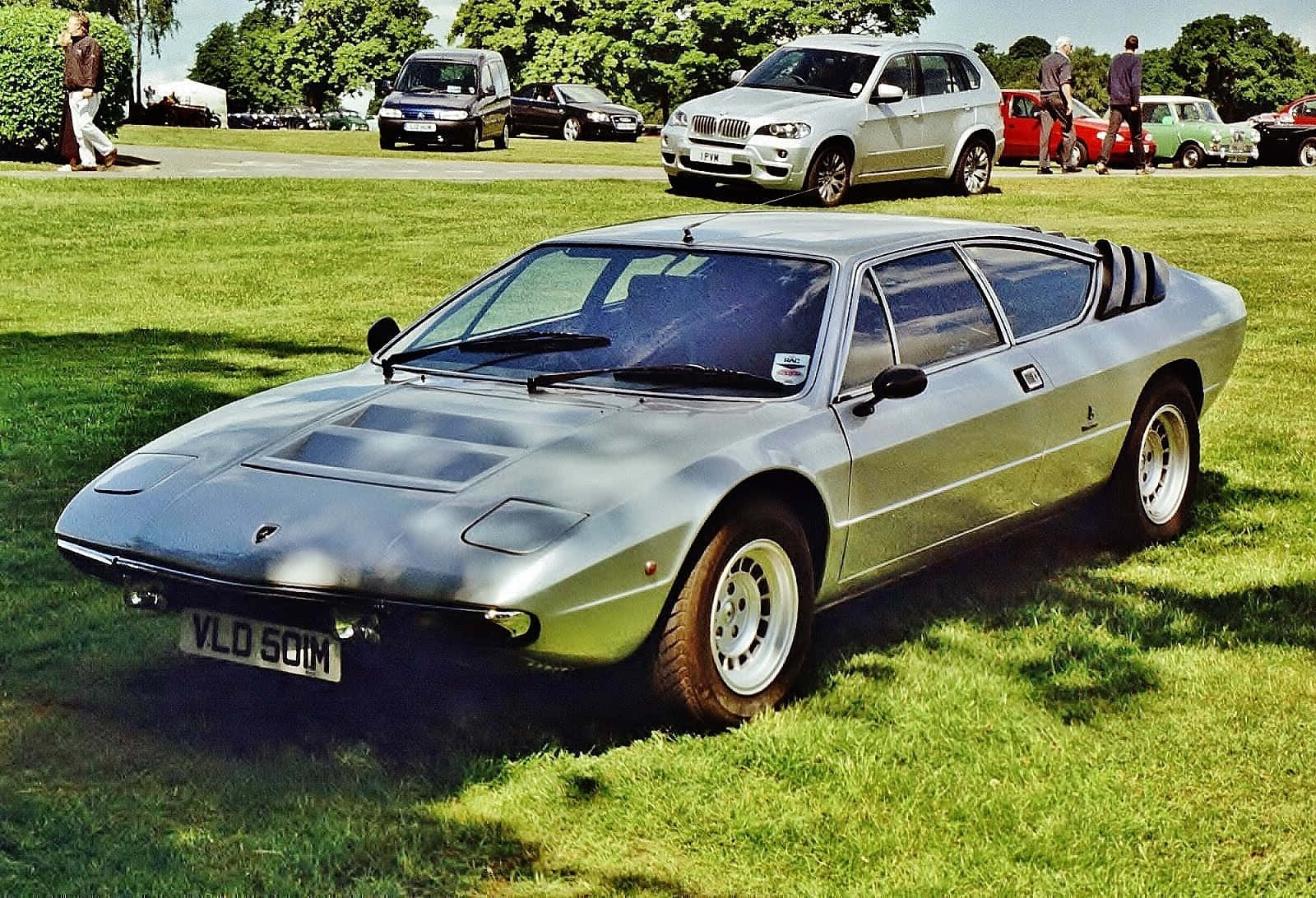 Lamborghini Urraco 桌布 壁紙 — 一架流線型的銀色林寶堅尼Countach停泊在經典車展的翠綠草地上，背景有其他車輛和人群。