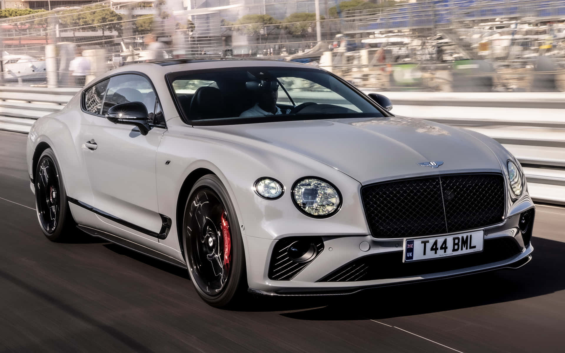 Bentley Continental Gt 桌布 壁紙 — 一架流線型的銀色賓利 Continental GT 在賽道上疾馳，背景是模糊的看台。