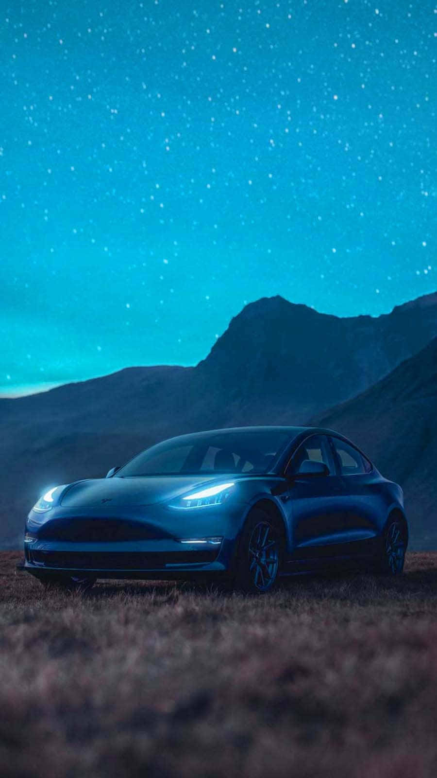 tesla 桌布 壁紙 — 一架流線型藍色 Tesla Model 3 停泊在草地上，背景係星空同黑暗嘅山脈。
