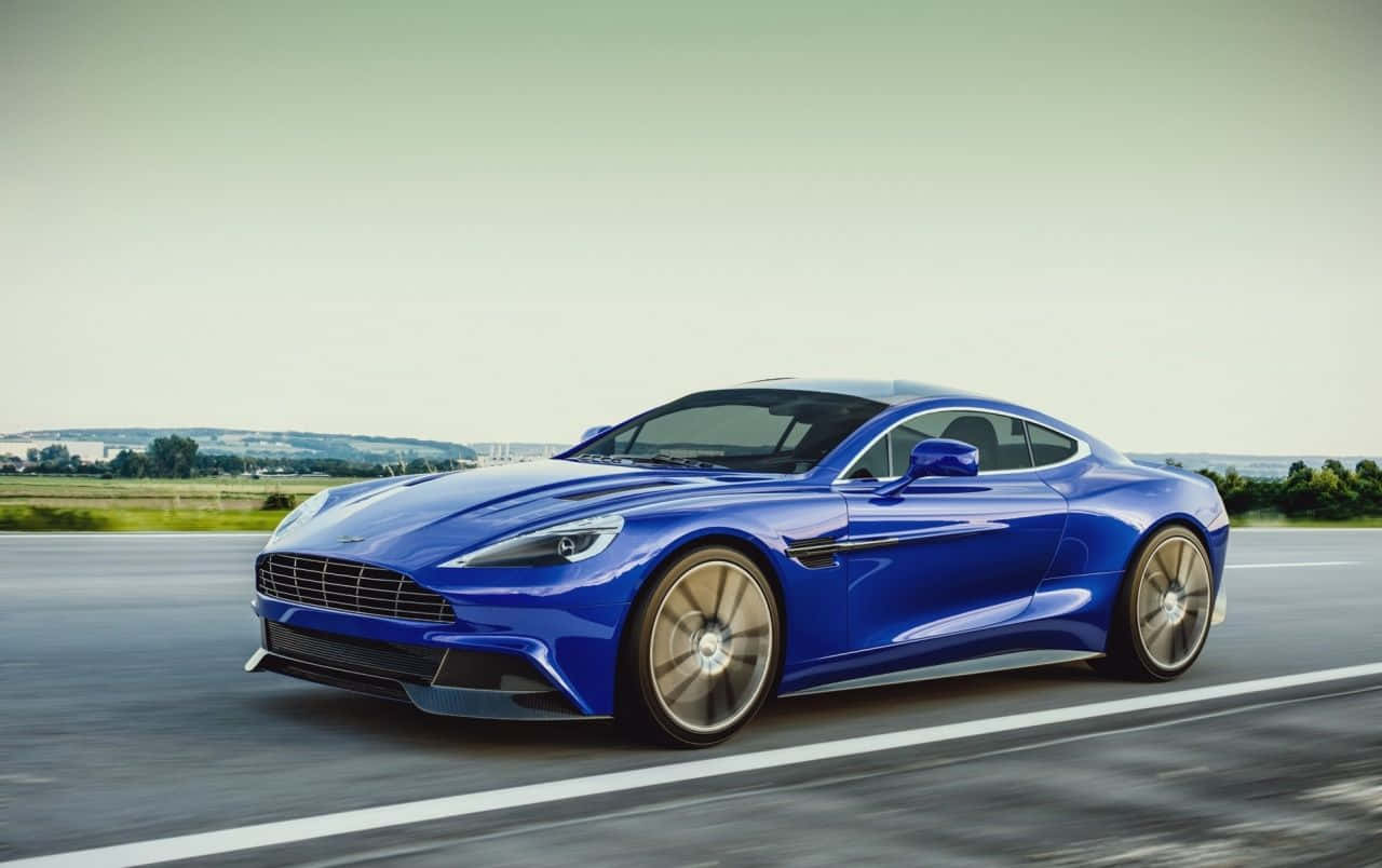 Aston Martin Vanquish 桌布 壁紙 — 一架流線型藍色Aston Martin跑車在柔和陰天下沿鄉村高速公路飛馳。