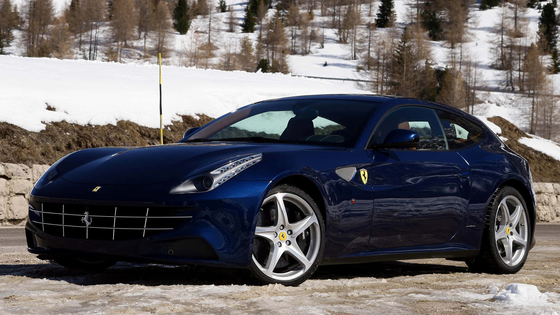 Ferrari Ff 桌布 壁紙 — 一架流線型藍色法拉利跑車停泊在積雪的路邊，背景是白雪覆蓋的樹木和山丘。