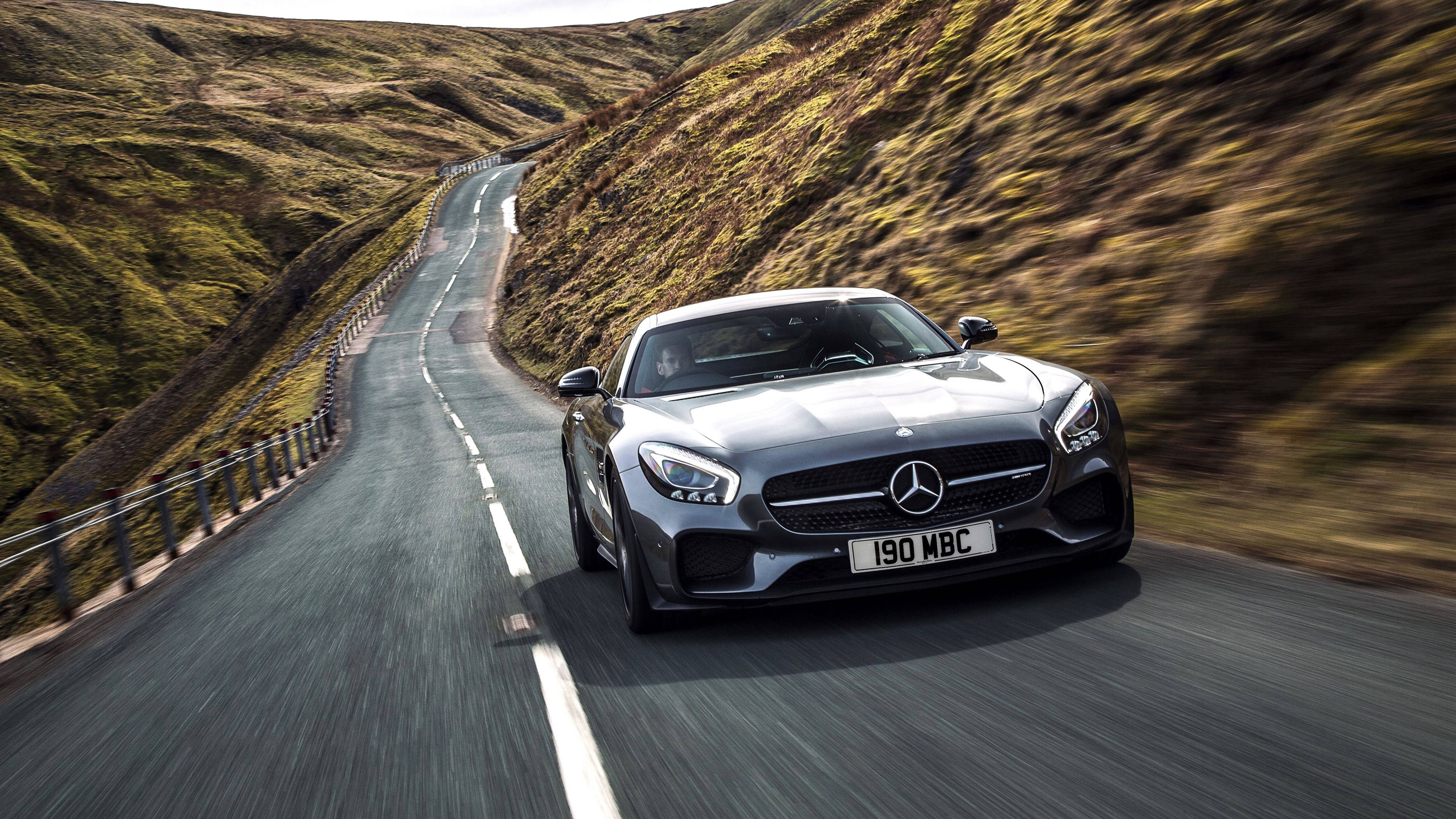 Cool Car 桌布 壁紙 — 一架流線型銀色 Mercedes-AMG GT S 沿著蜿蜒的山路疾馳，兩旁模糊的綠色山丘一閃而過。