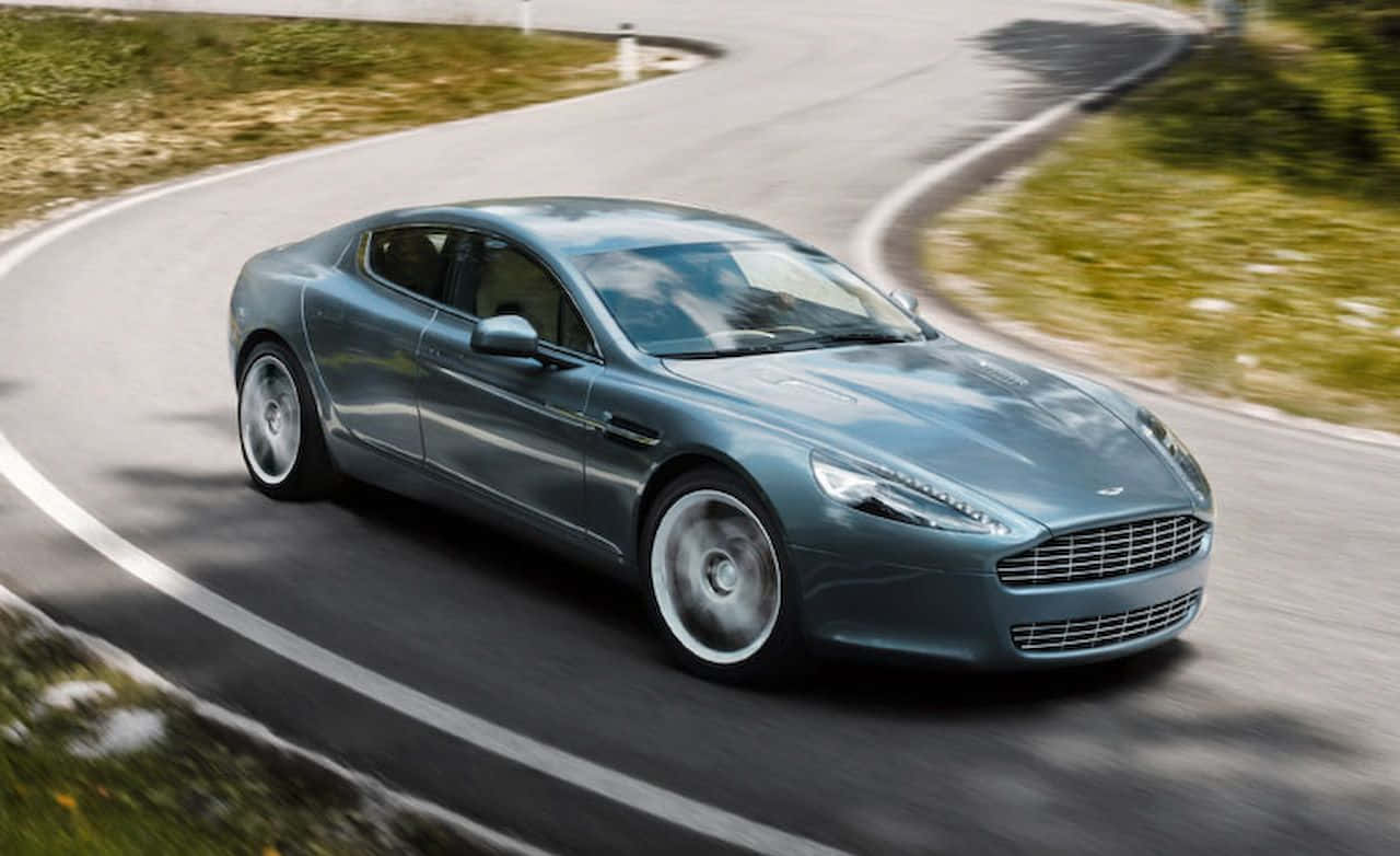 Aston Martin Rapide S 桌布 壁紙 — 一架流線型銀色Aston Martin沿著蜿蜒的山路疾馳，周圍的綠植和瀝青路面模糊不清。