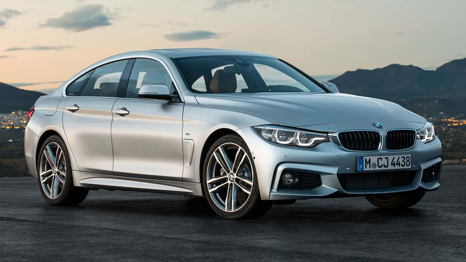 Bmw 4 Series 桌布 壁紙 — 一架流線型銀色BMW 4 Series Coupe停泊在昏暗的道路上，暮色中群山和城市燈光閃爍。