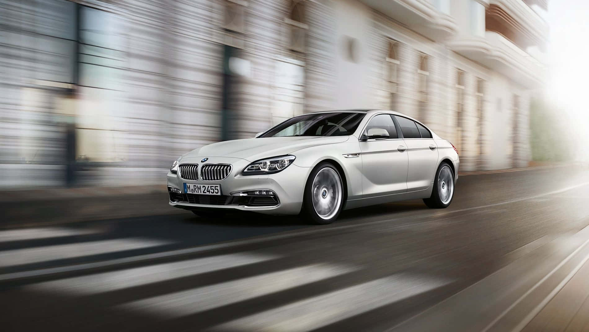 Bmw 6 Series 桌布 壁紙 — 一架流線型銀色寶馬6系房車在陽光普照的都市街道上飛馳，背景建築物因動態模糊而拖曳成線。