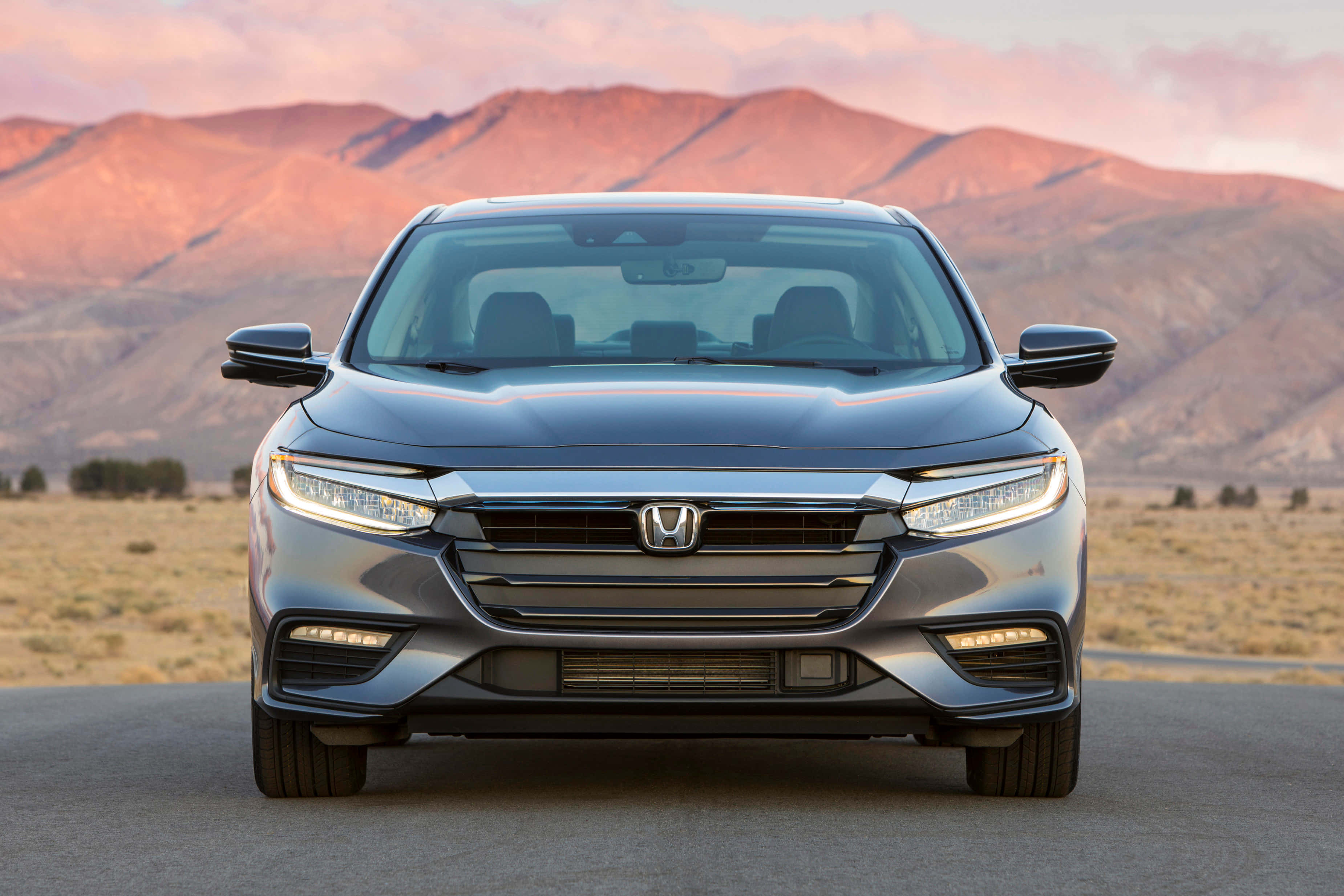 Honda Insight 桌布 壁紙 — 一架流線型銀色本田房車在沙漠公路上向前行駛，背後是粉紅色和橙色夕陽照耀的山巒。