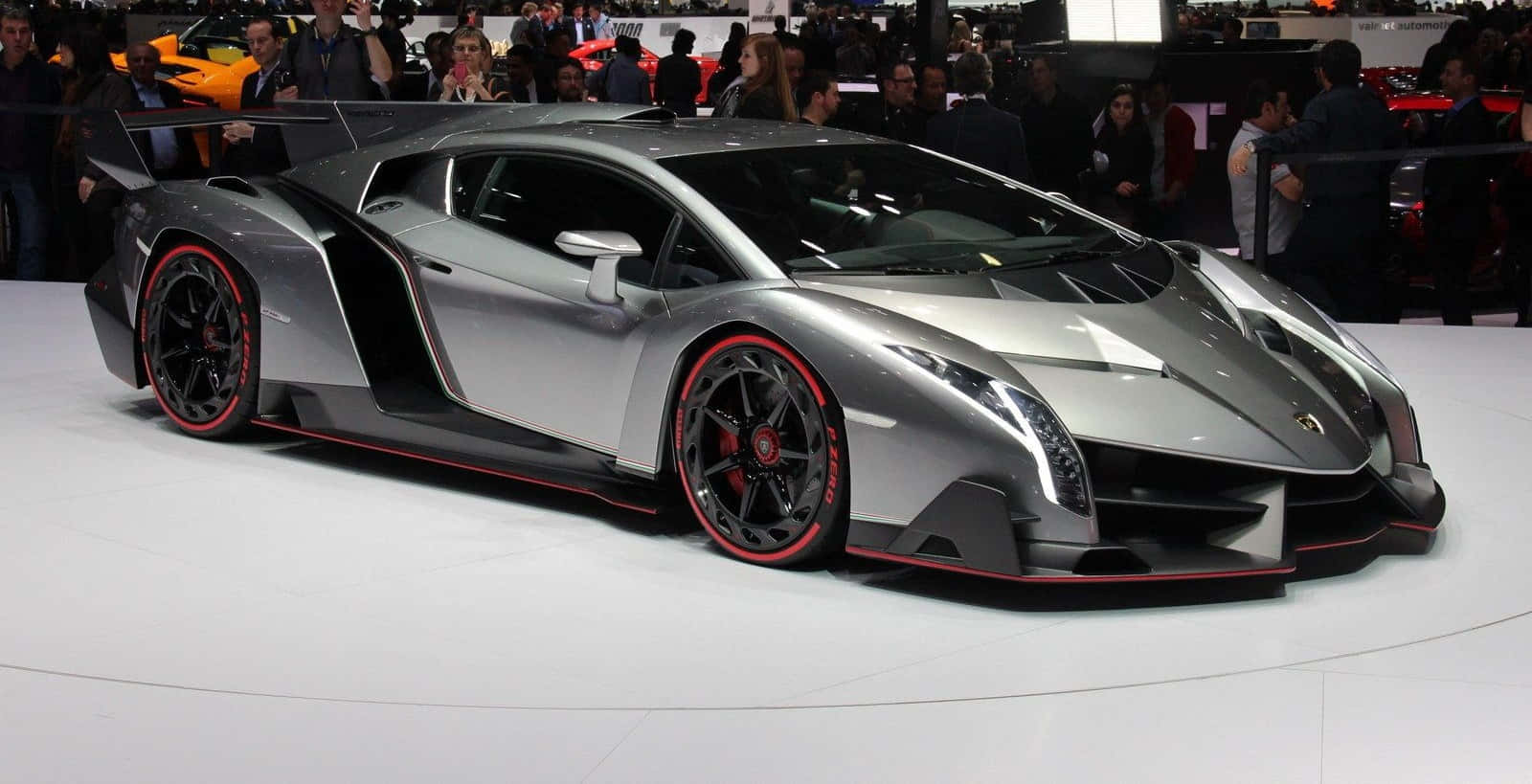 Lamborghini Veneno 桌布 壁紙 — 一架流線型銀色林寶堅尼 Veneno 配以紅色輪圈，在車展上展出，周圍人群簇擁。