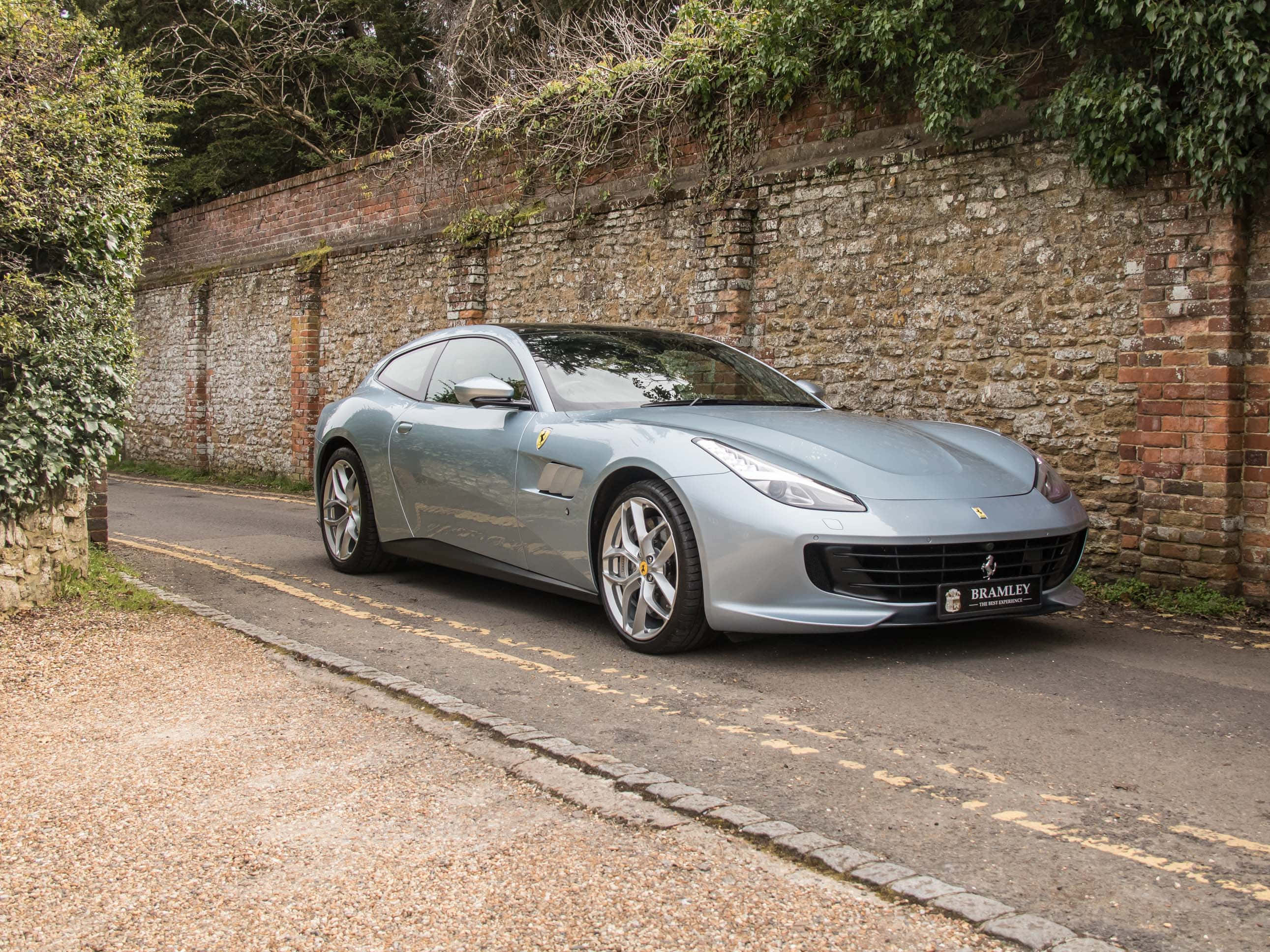 Ferrari Gtc4lusso 桌布 壁紙 — 一架流線型銀色法拉利 GTC4Lusso 停泊在寧靜的道路上，旁邊是長滿青苔的石牆，常春藤攀爬而上。