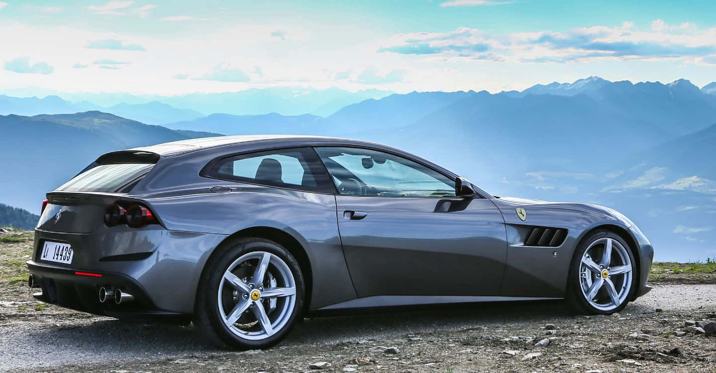 Ferrari Gtc4lusso 桌布 壁紙 — 一架流線型銀色法拉利停泊喺山頂觀景點，背景係分層嘅藍色山峰，天空局部多雲。