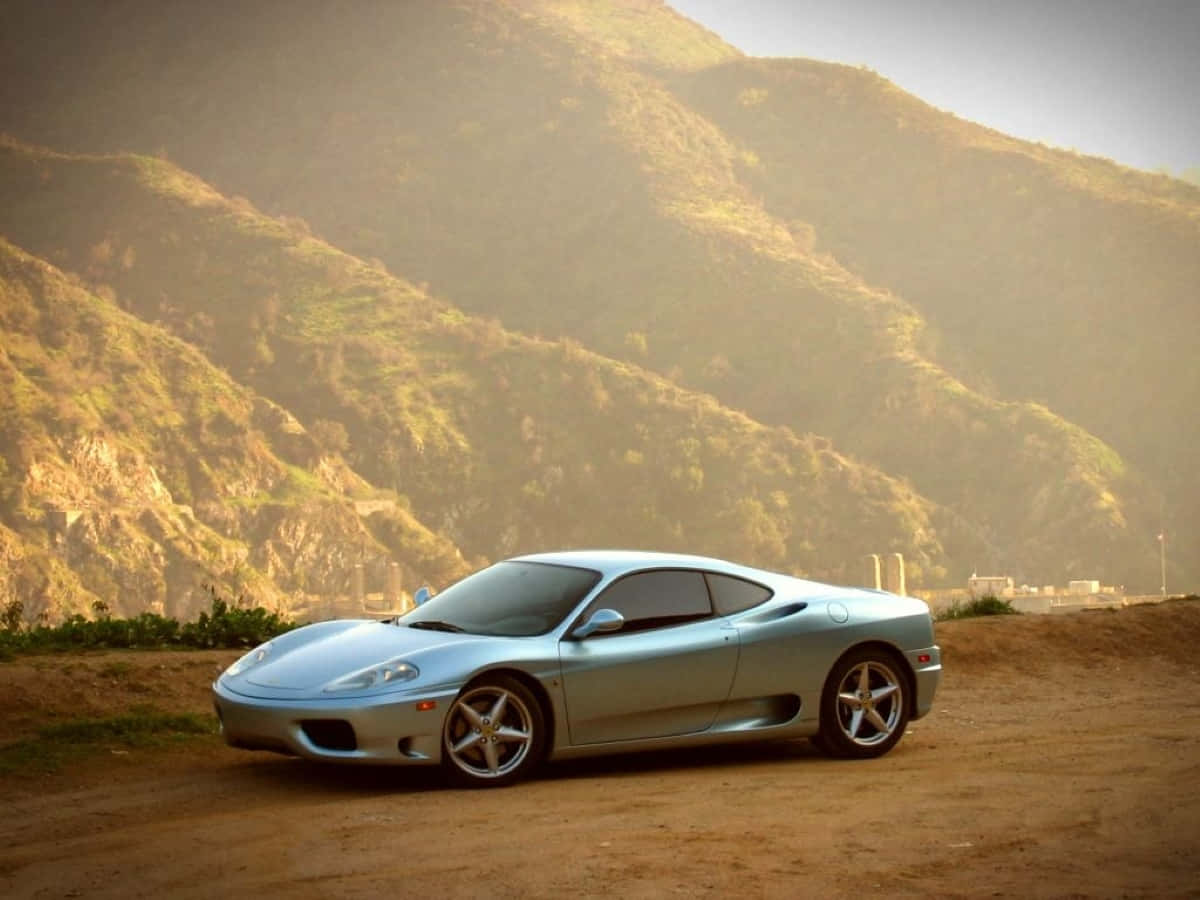 Ferrari 360 Modena 桌布 壁紙 — 一架流線型銀色跑車停泊在塵土飛揚的路邊，背景是陽光普照的連綿山丘。